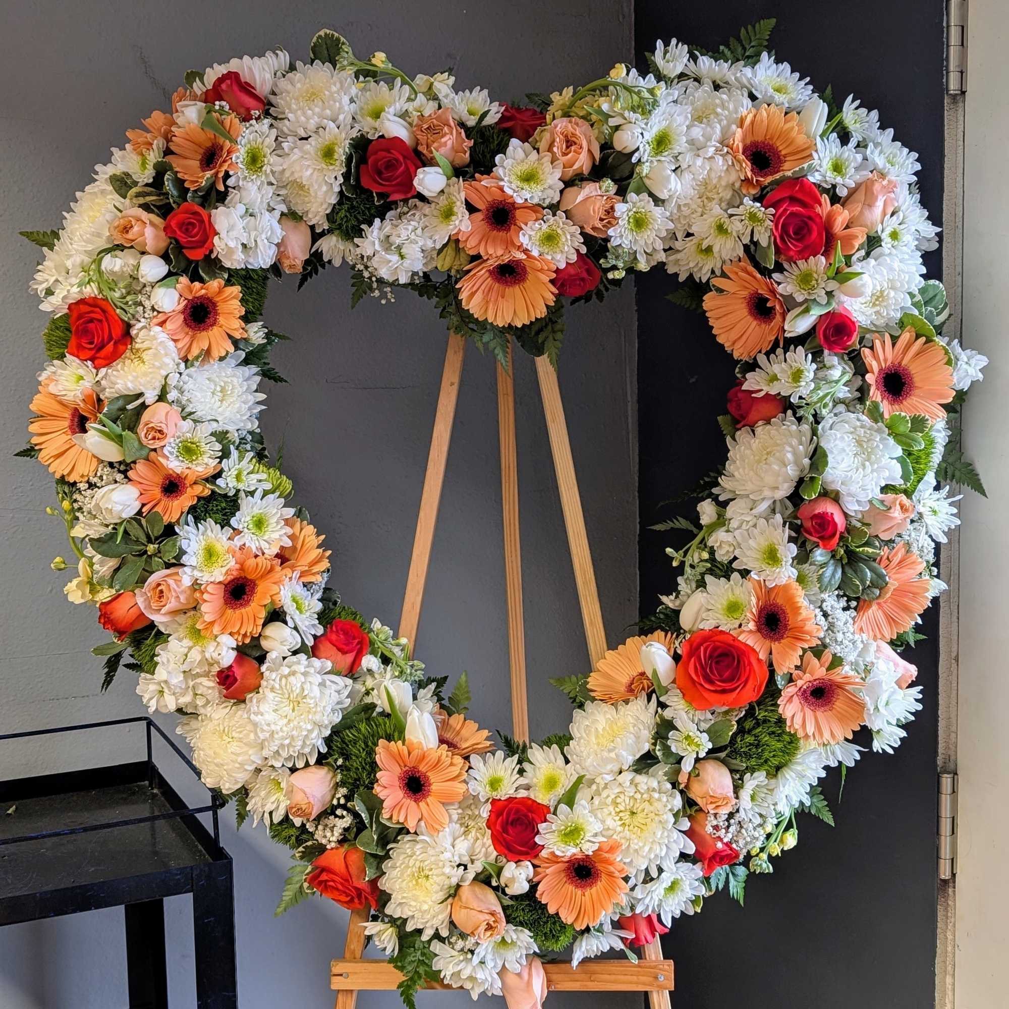 Heart-shaped floral wreath on an easel with roses and daisies