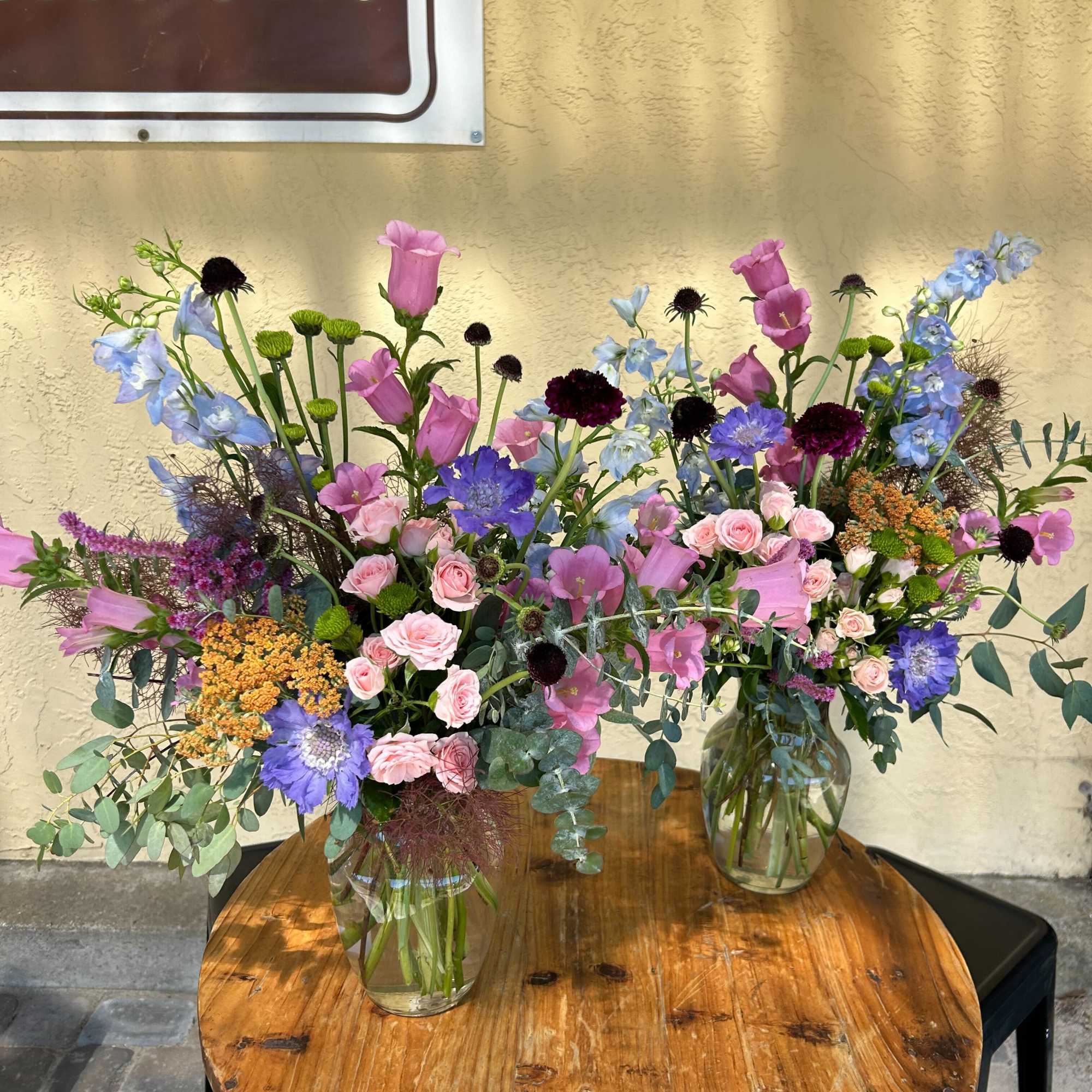 Two colorful mixed flower arrangements in glass vases on a wooden table