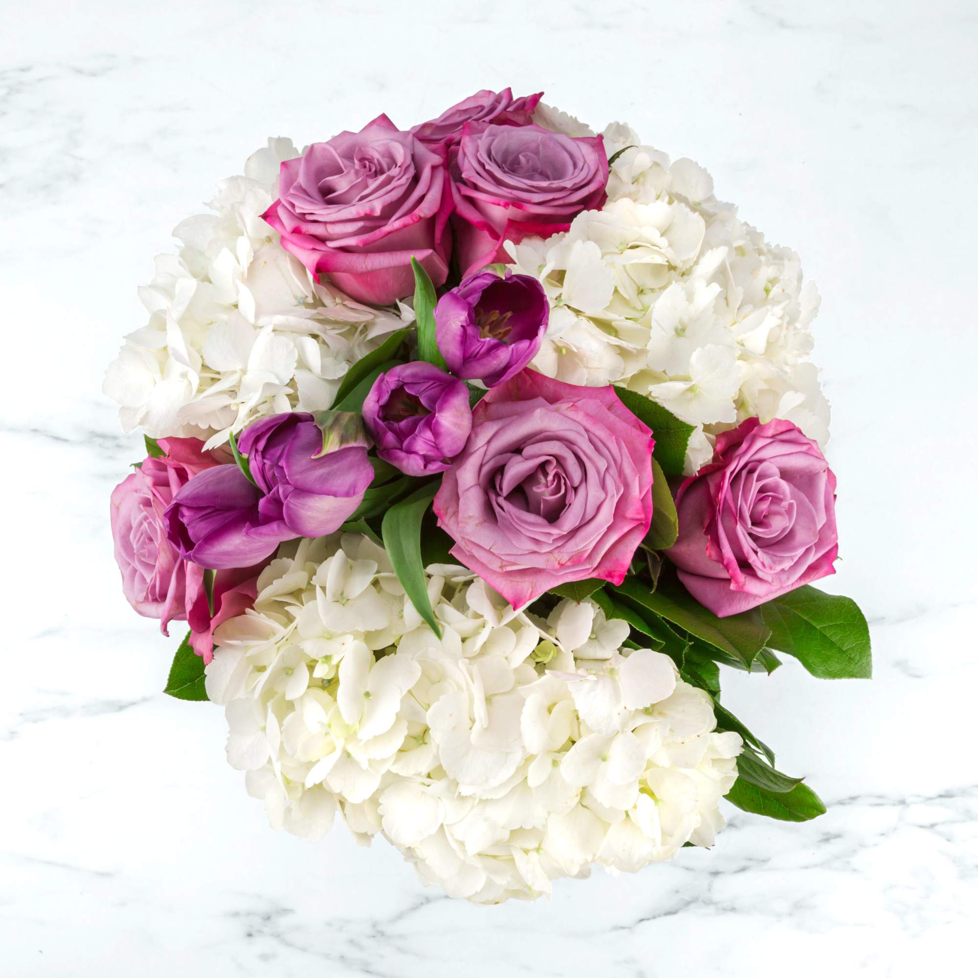 Round arrangement of lavender roses and purple tulips nestled in white hydrangeas