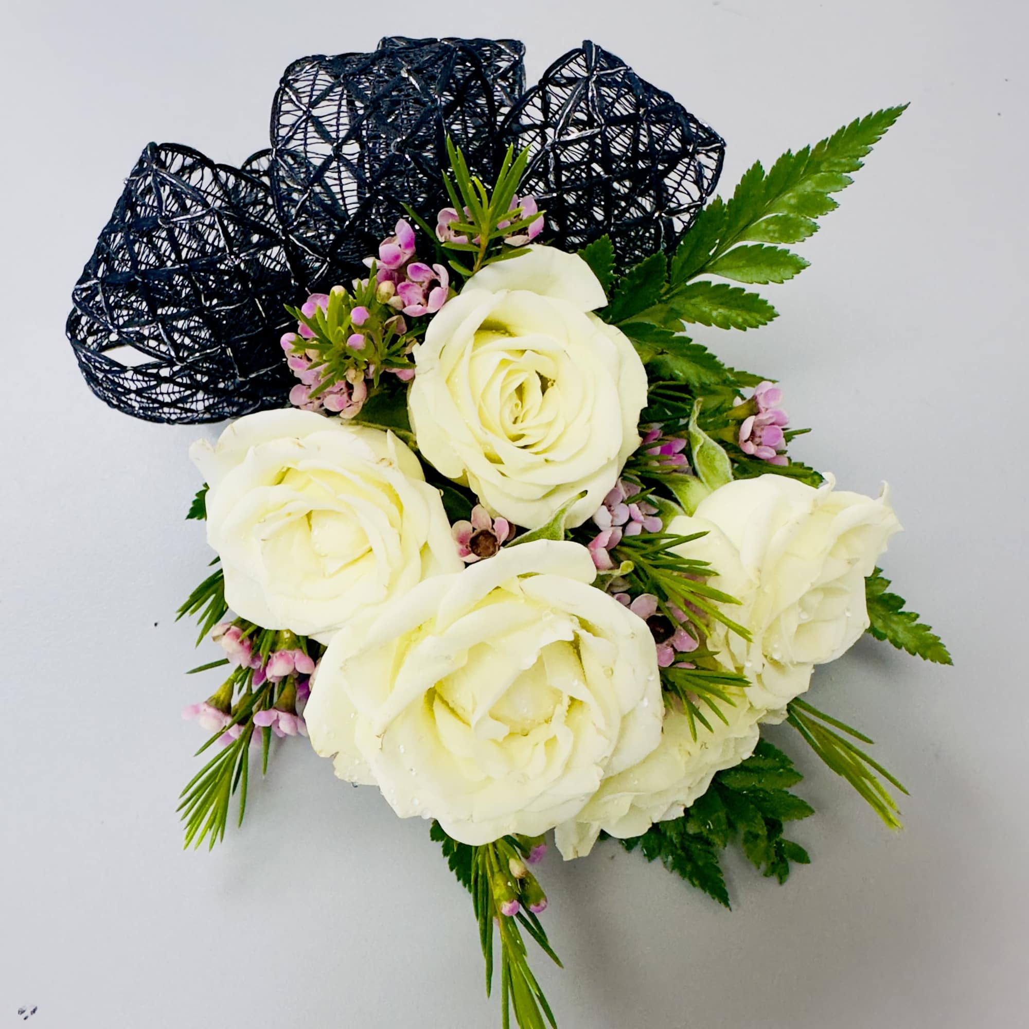 Creamy white roses clustered into a compact, hand-tied corsage give this wrist