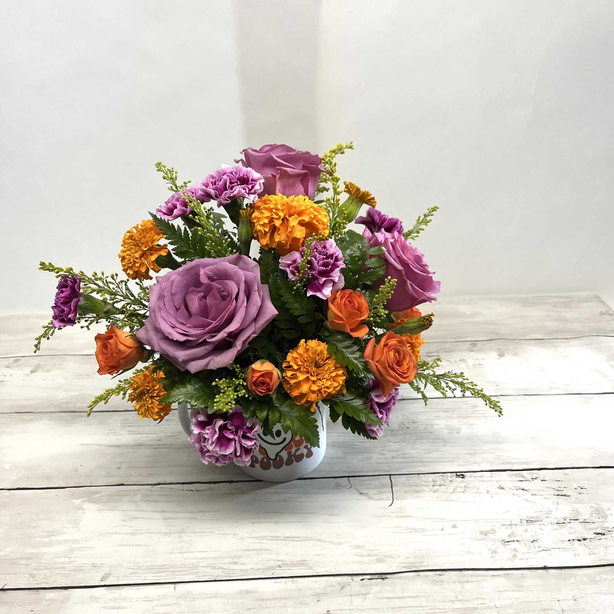 Mixed bouquet of purple roses and orange carnations in a white mug