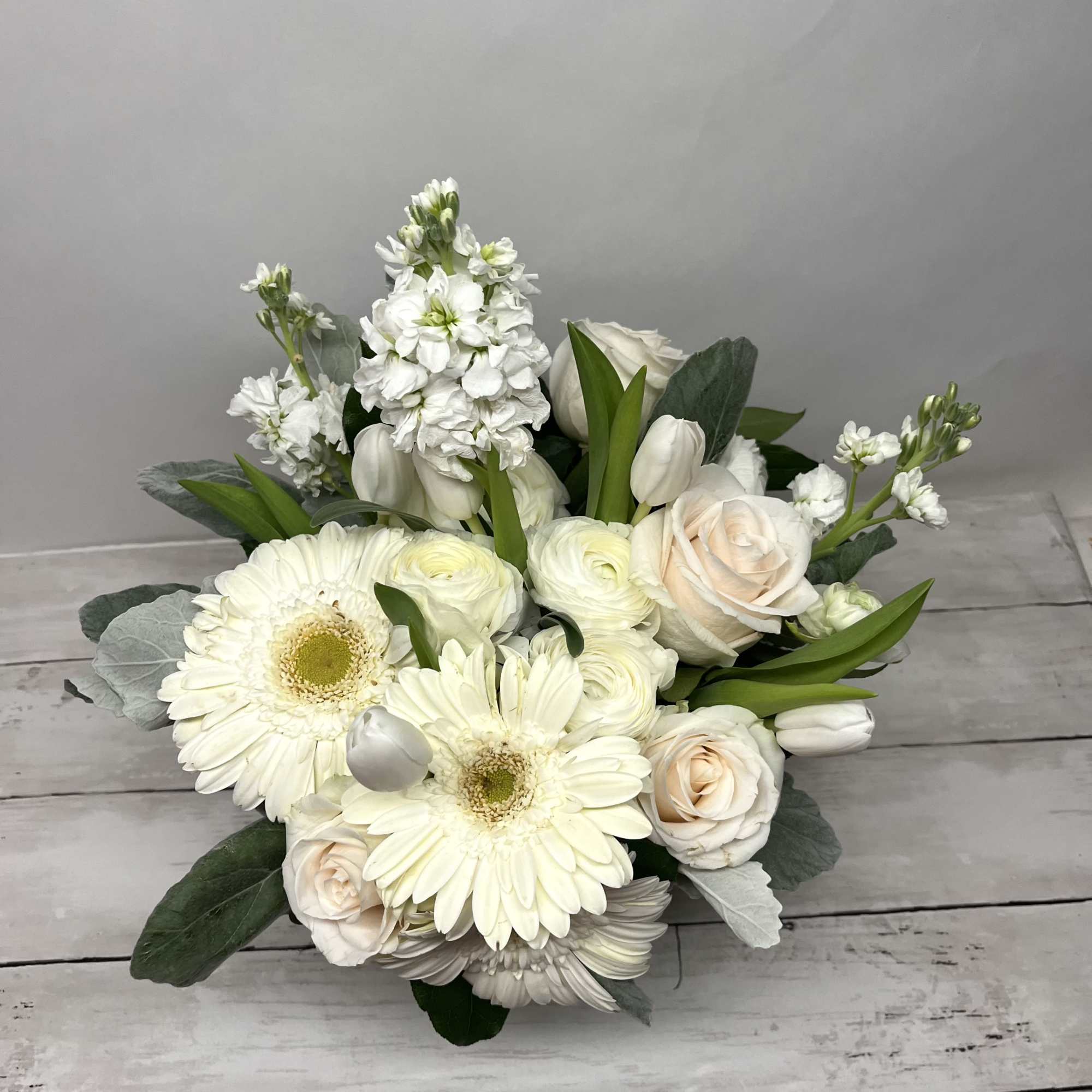 This arrangement contains gerbera daisies, roses, tulips, stock, and other seasonal blooms.