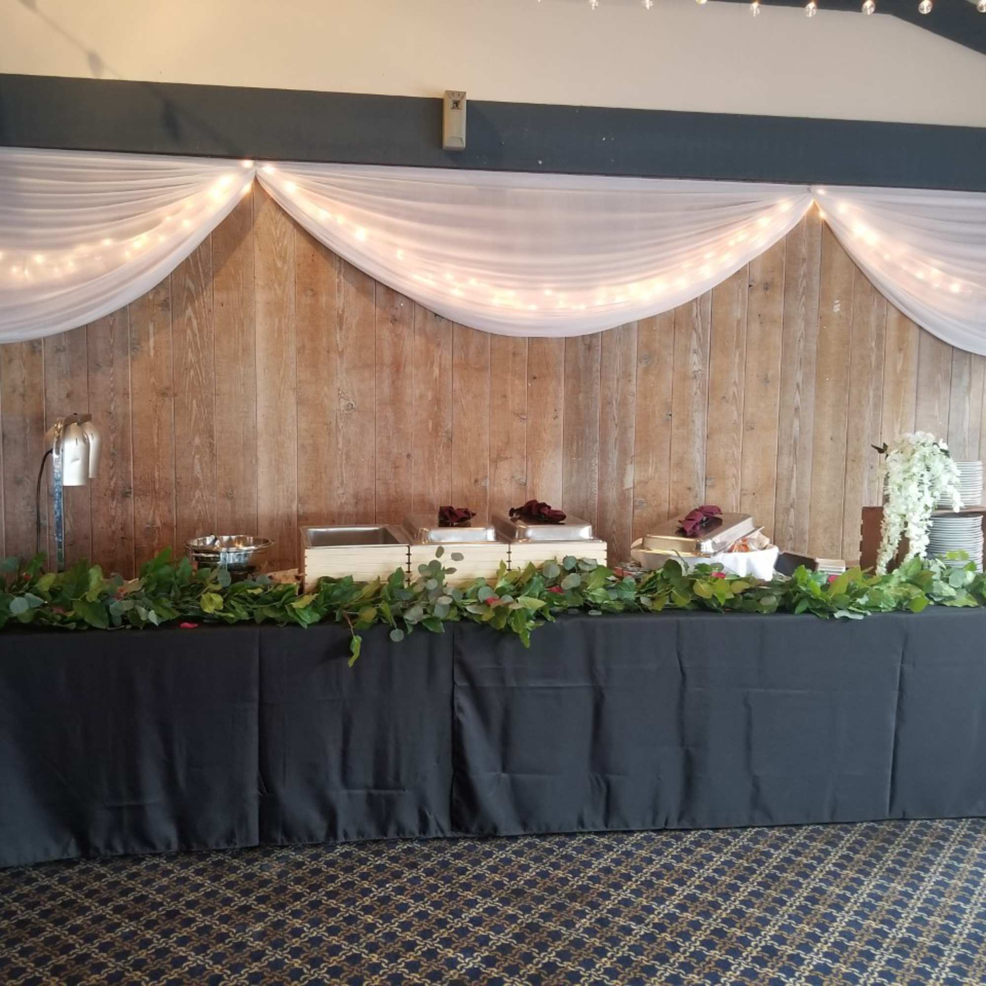 Buffet table with greenery garland and white draped backdrop with lights