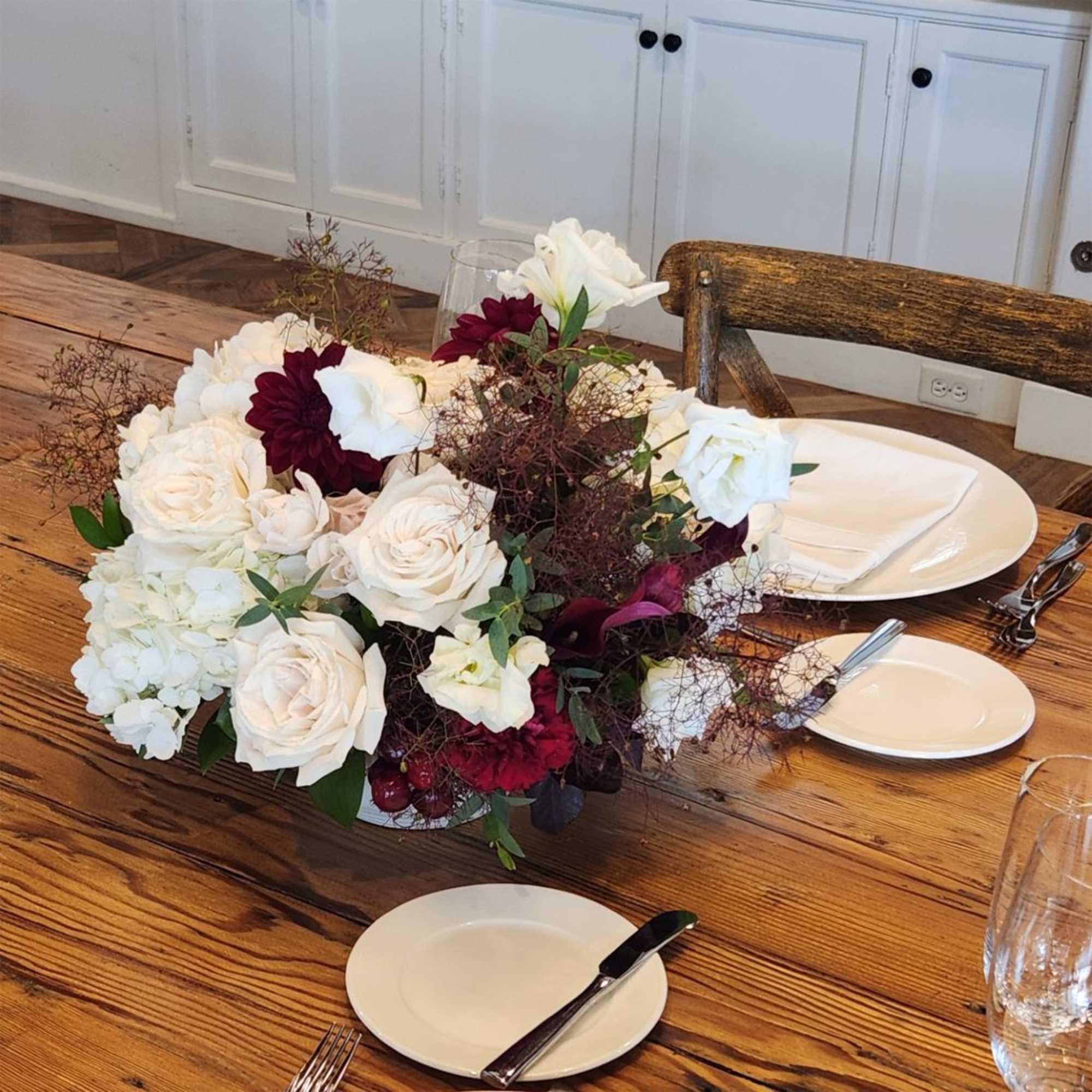 Low floral centerpiece with white roses and burgundy blooms on a dining table
