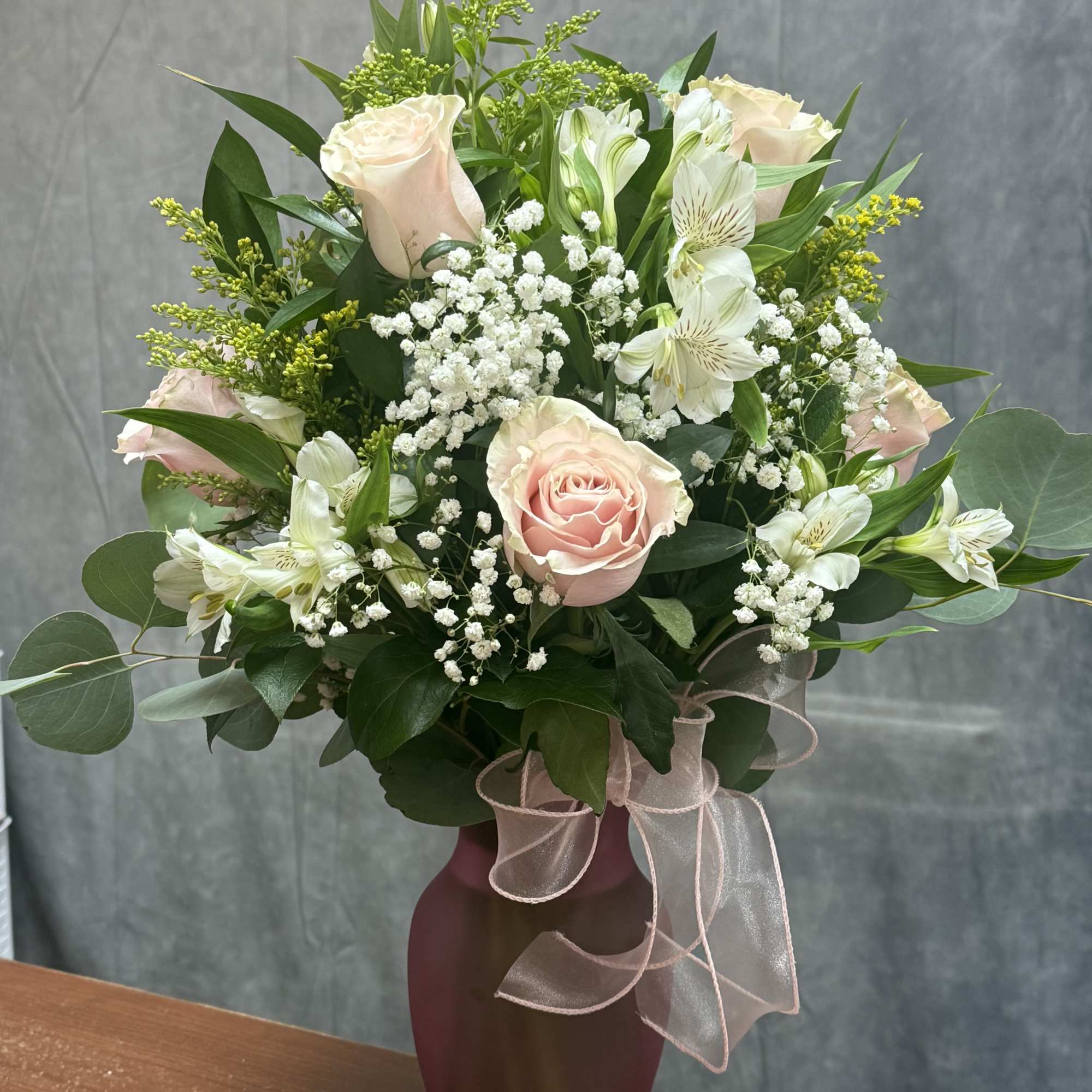 Tall arrangement of pale pink roses and white blooms in a pink frosted vase with ribbon bow