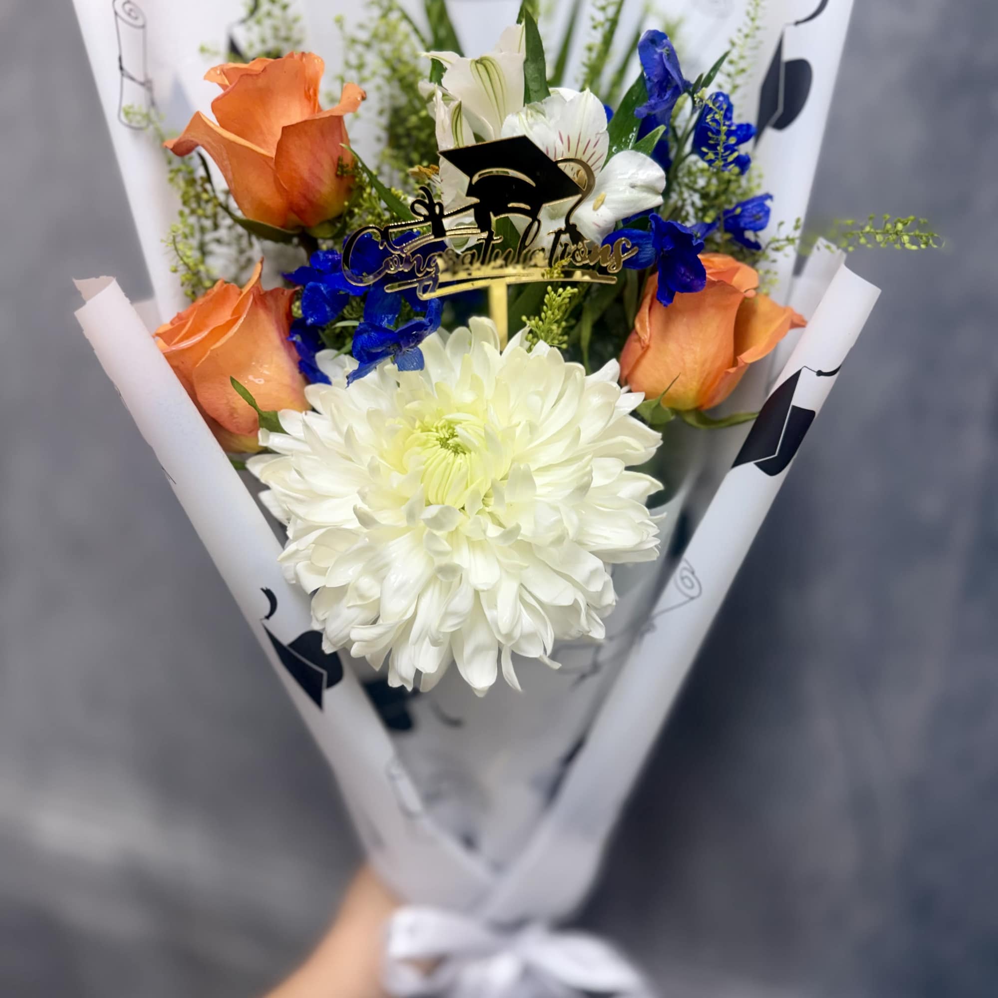 Bright orange roses with a large white chrysanthemum and vivid blue accents