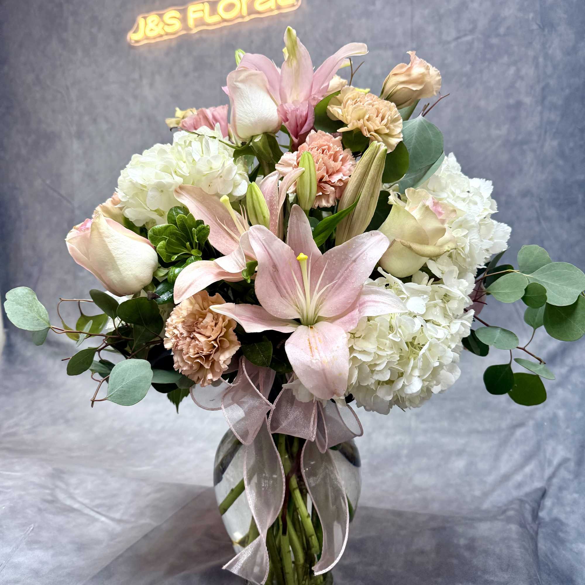 Pink lilies and white hydrangeas in a glass vase with a ribbon