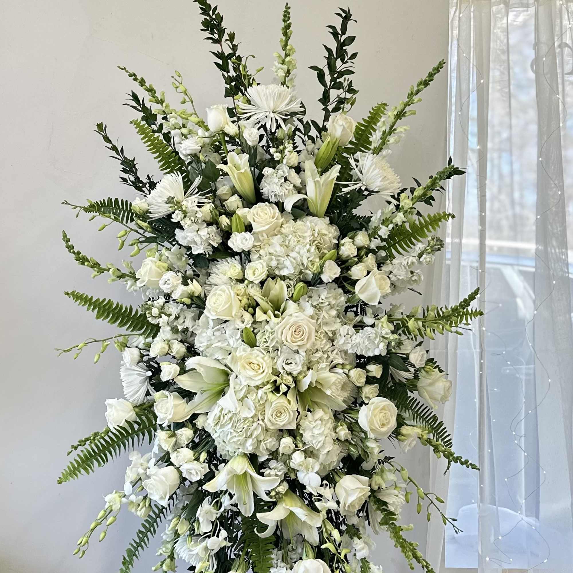 Tall white floral standing arrangement with roses and lilies on a black stand