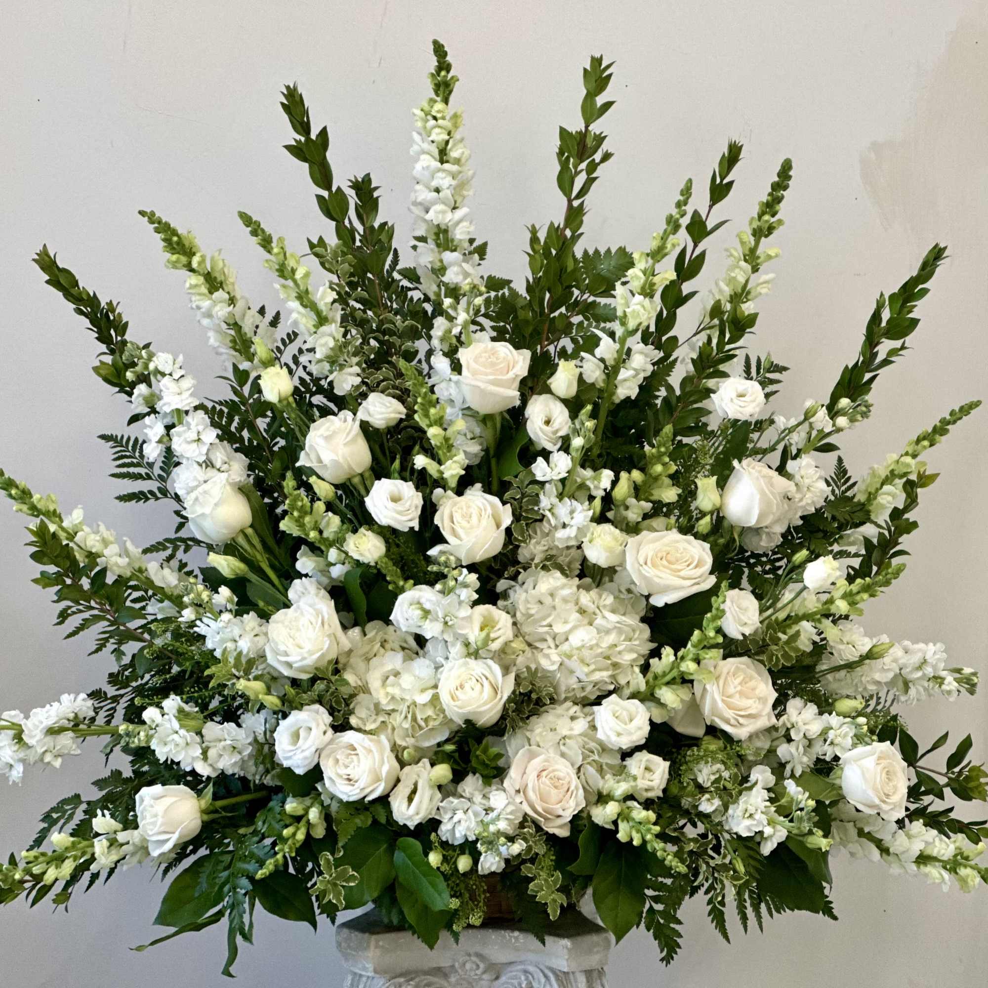 Large fan-shaped arrangement of white roses and other white flowers in a pedestal vase