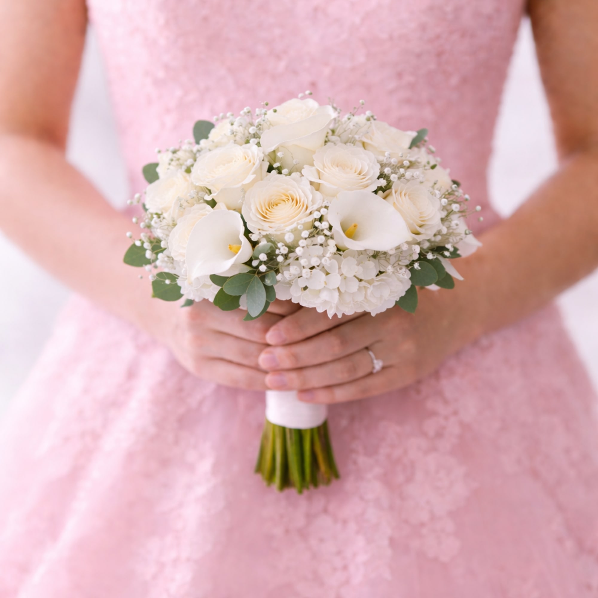Hand-tied bouquet of white roses and calla lilies held by a person in a pink lace dress