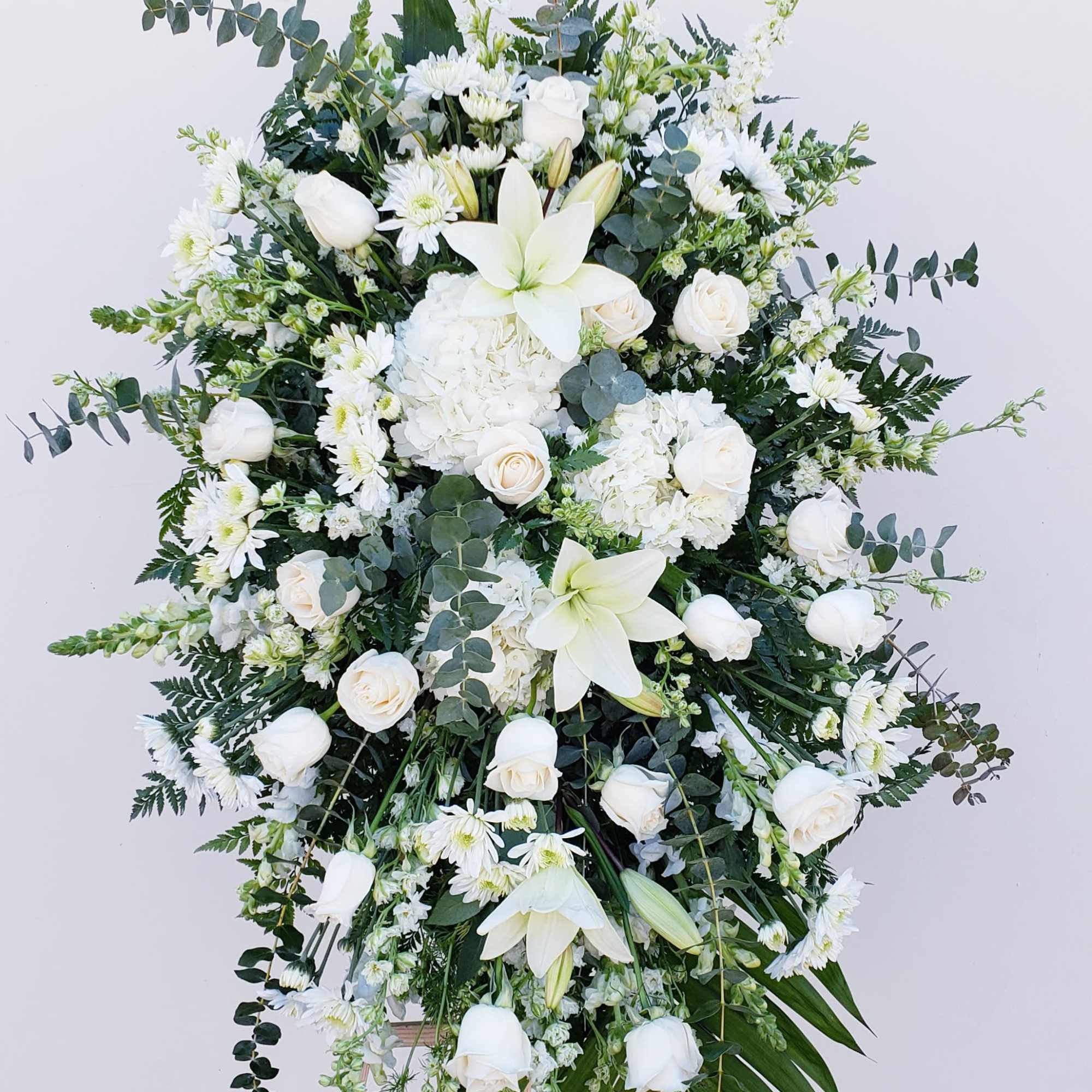 Large white floral standing spray with lilies, roses, and daisies