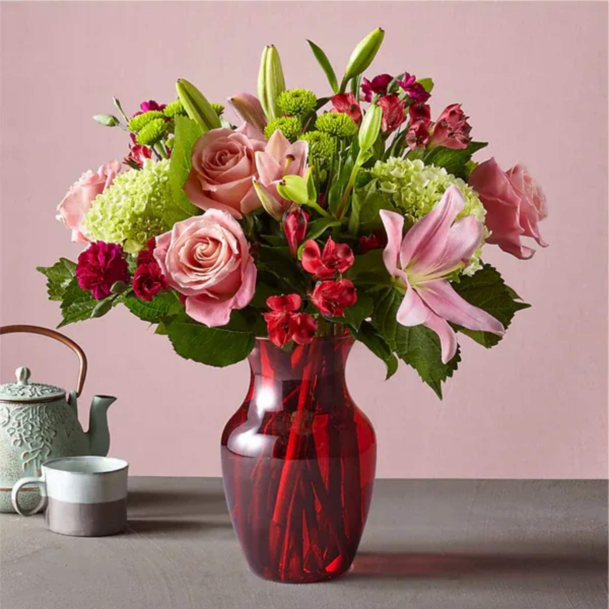 Pink roses and lilies arranged in a red glass vase