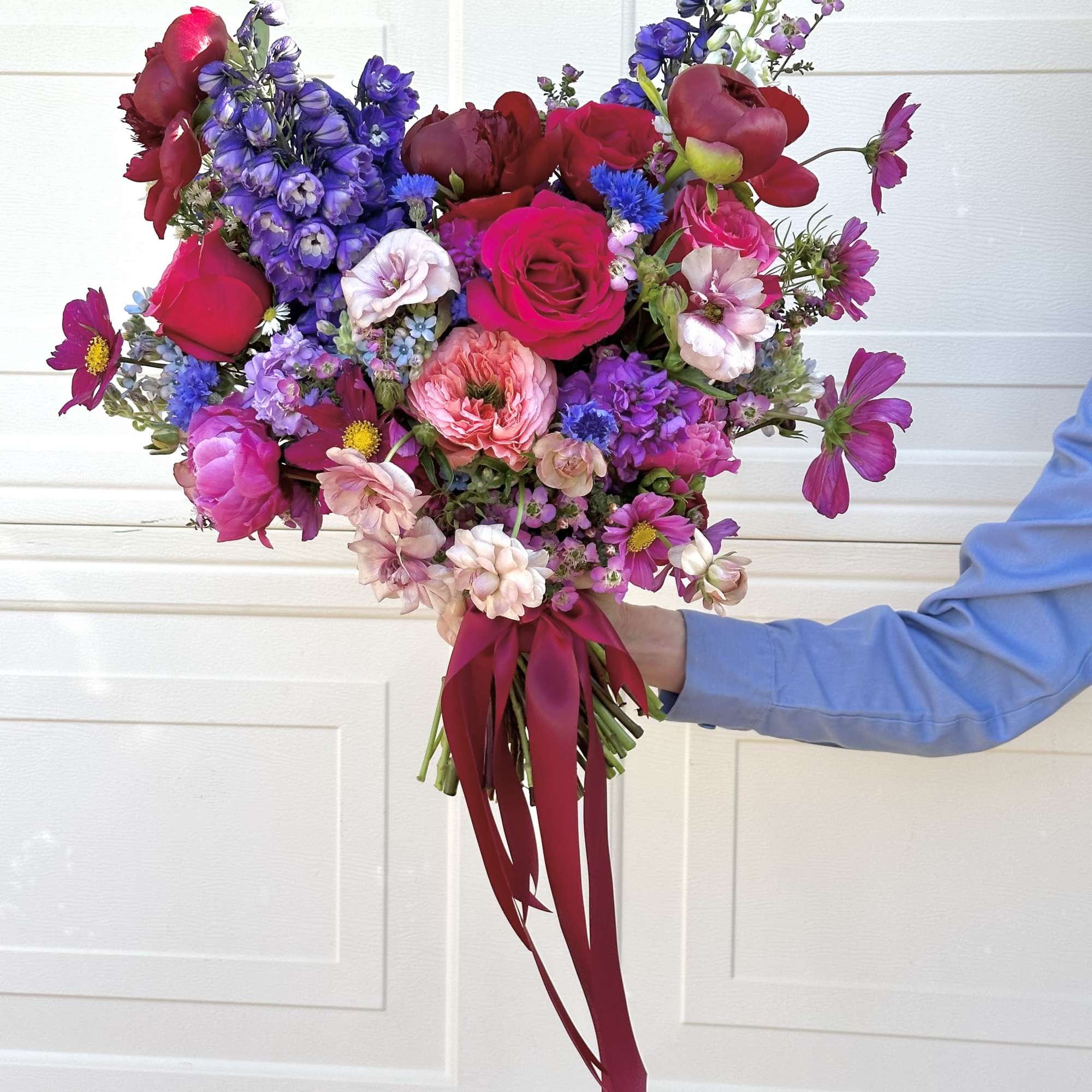 Handheld bouquet of pink, red, and purple flowers tied with a burgundy ribbon.
