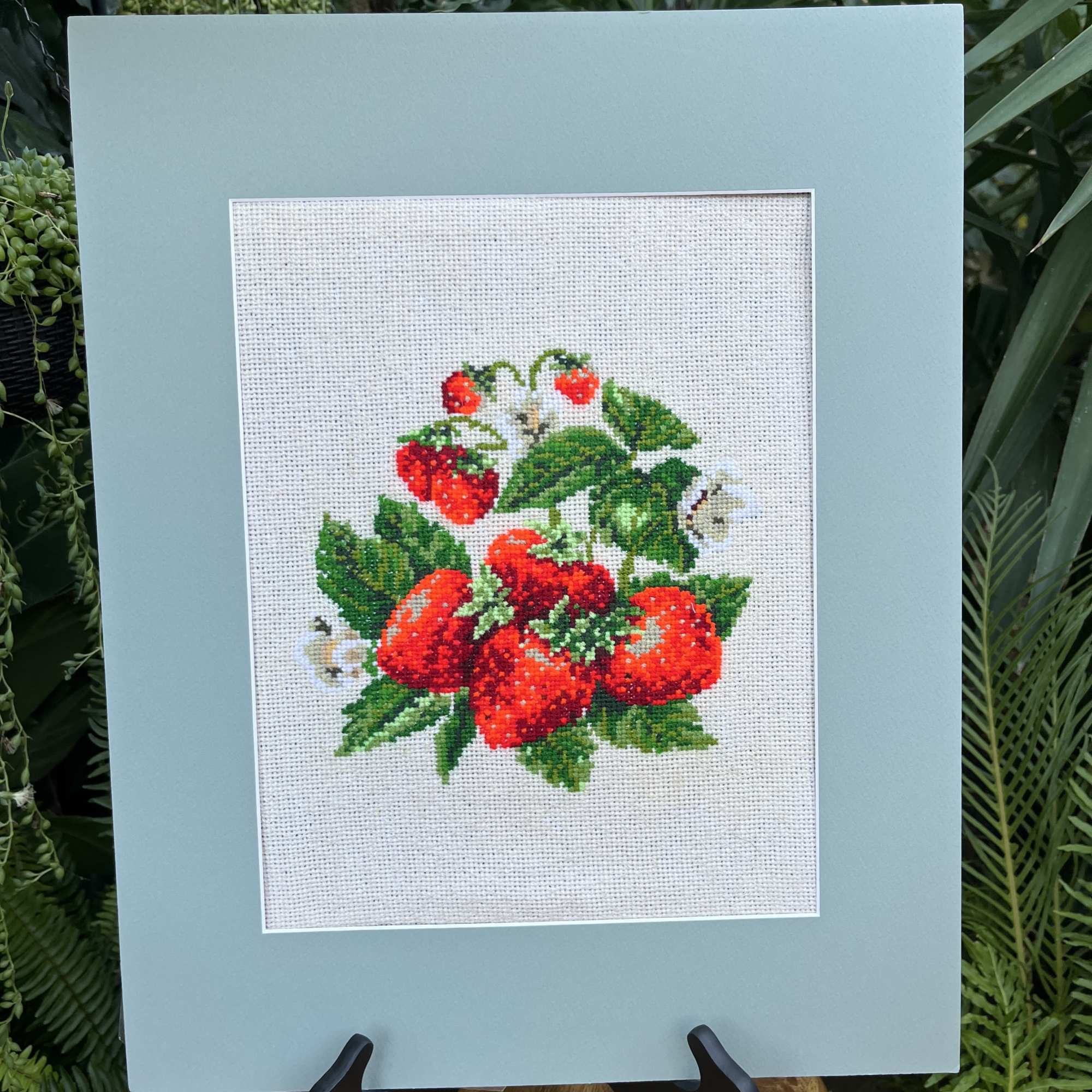 Framed cross-stitch of red strawberries and green leaves