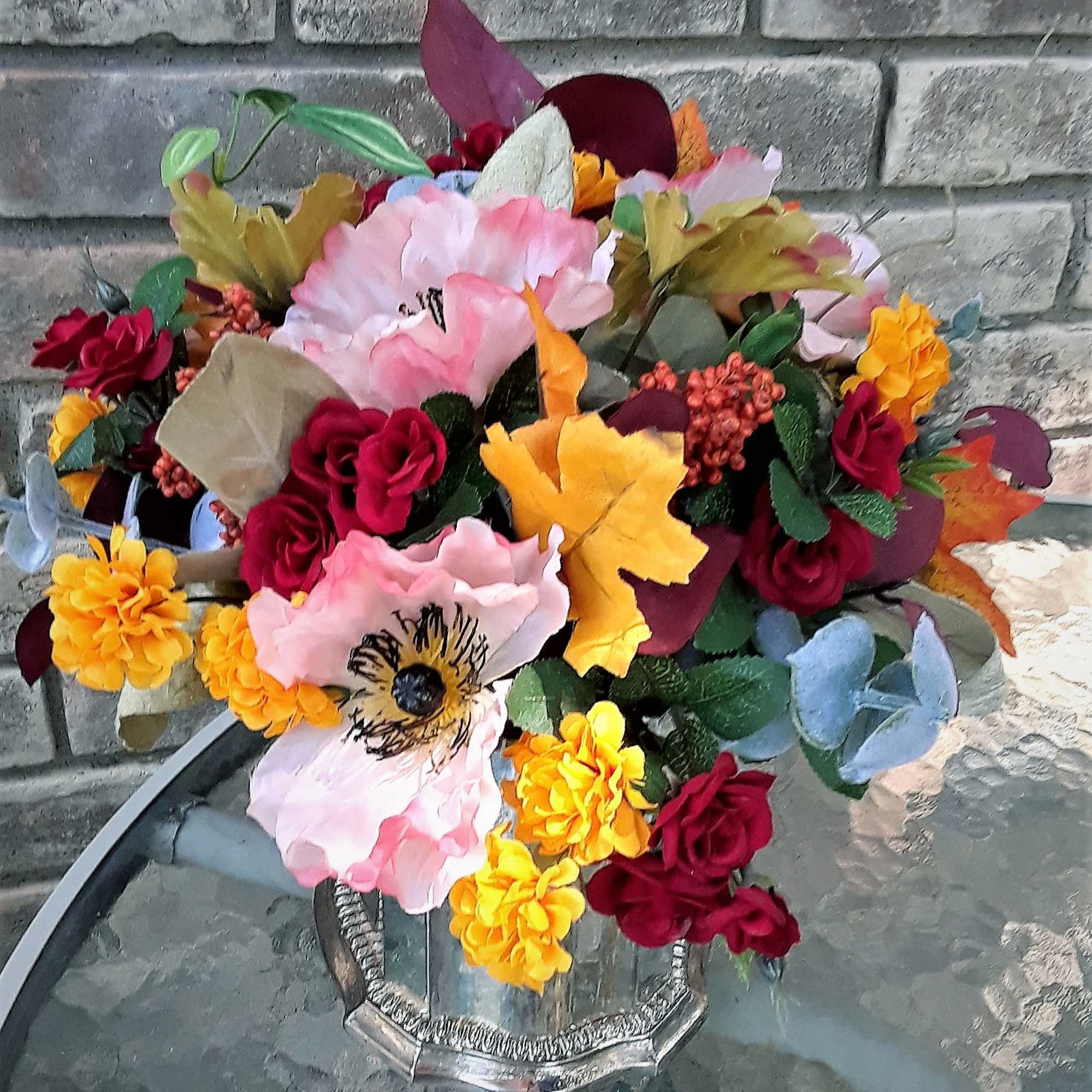 Mixed bouquet of pink, red, yellow, and orange flowers in a silver vase