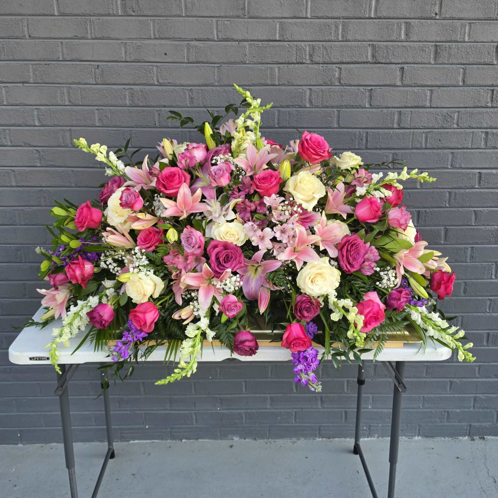 A sweeping casket spray designed for sympathy and memorial services, this large