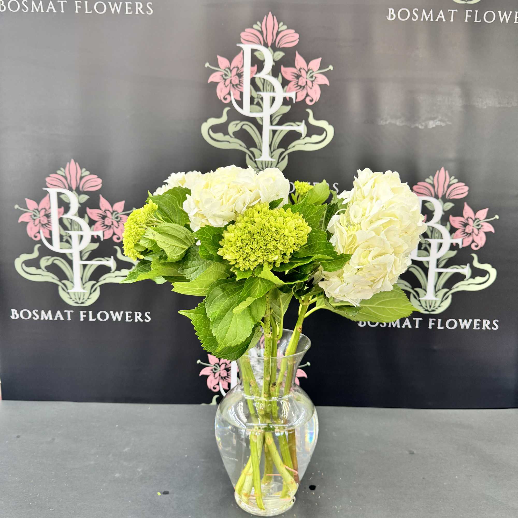 White hydrangeas and green blooms in a clear glass vase