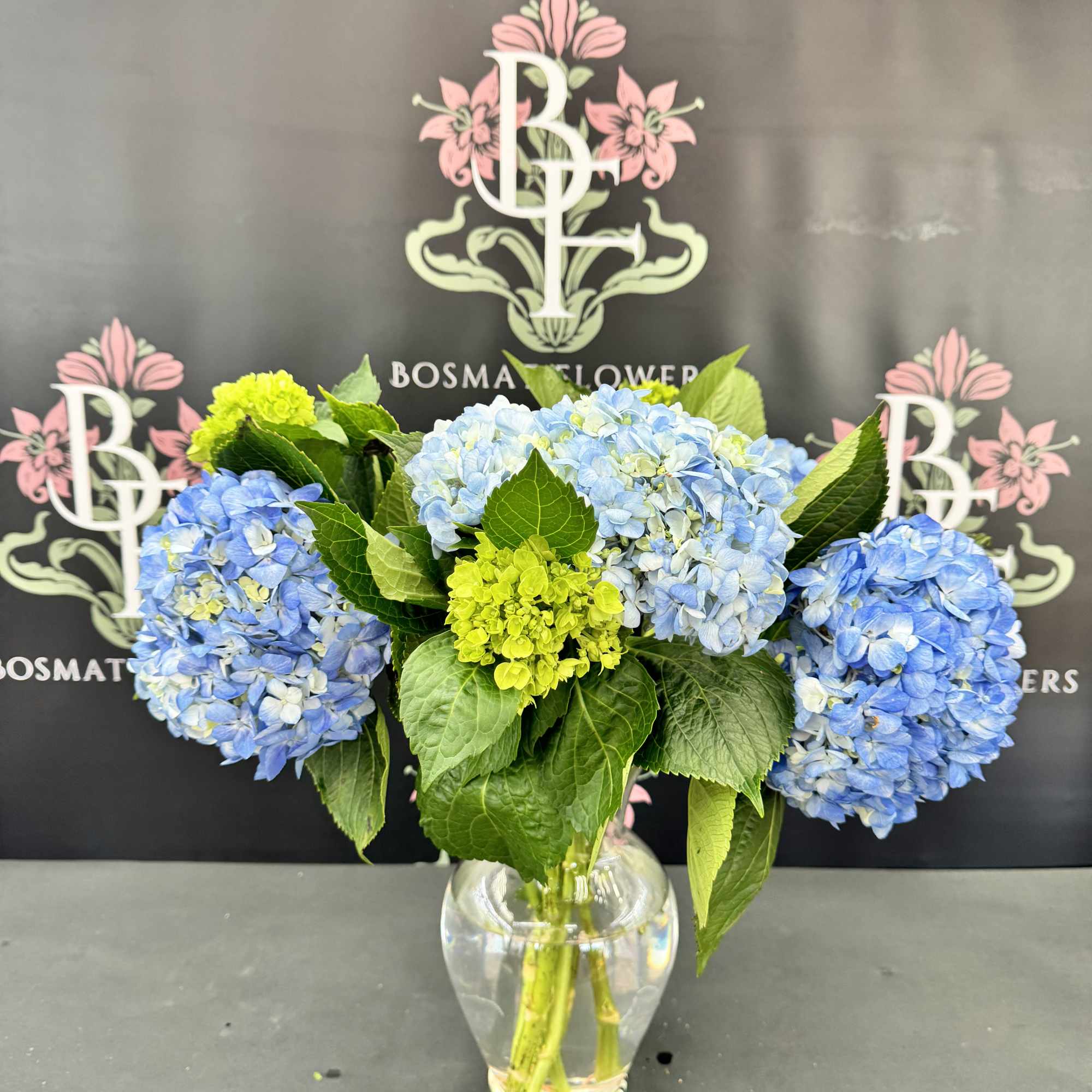 Blue hydrangeas and green blooms in a clear glass vase