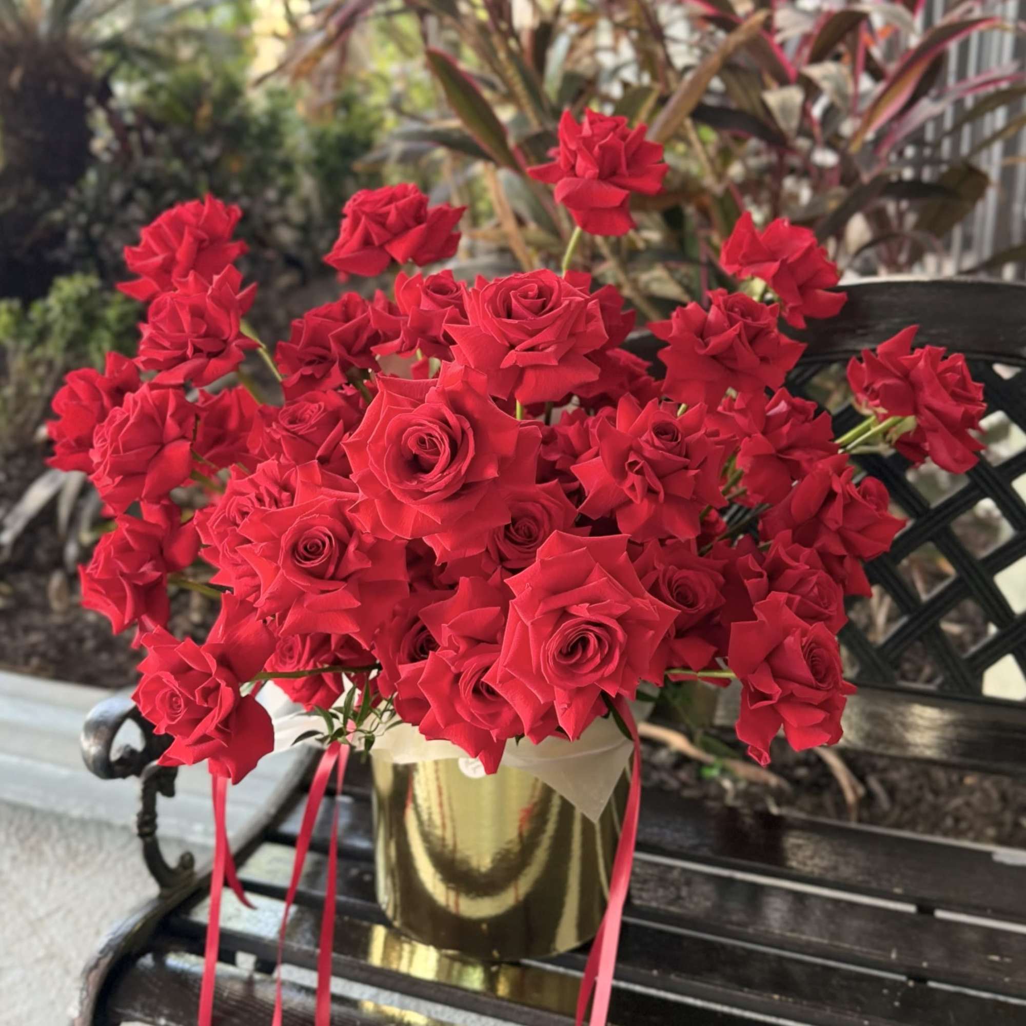 Velvet-red roses packed into a reflective gold cylindrical box create an immediate