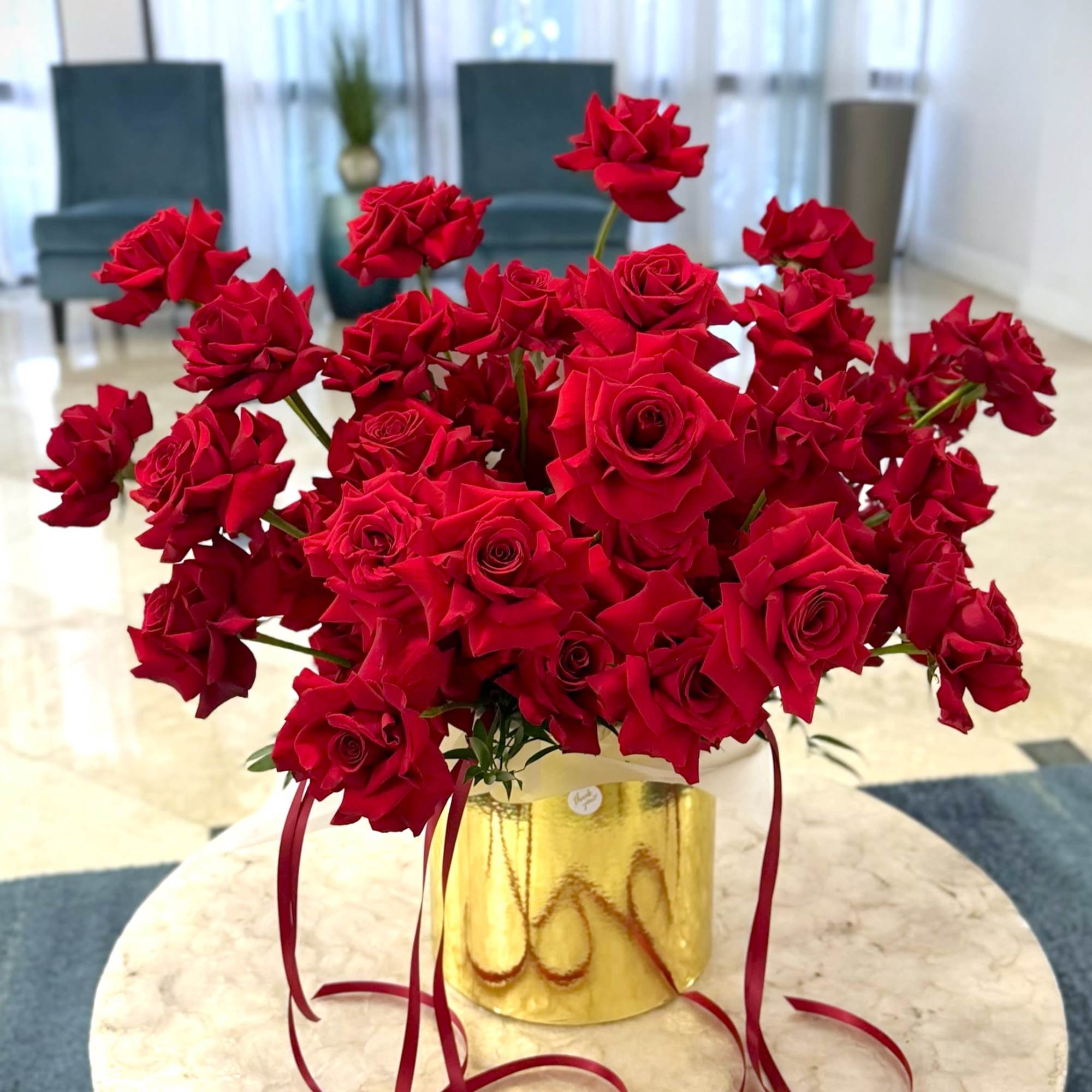 Velvet-red roses packed into a reflective gold cylindrical box create an immediate