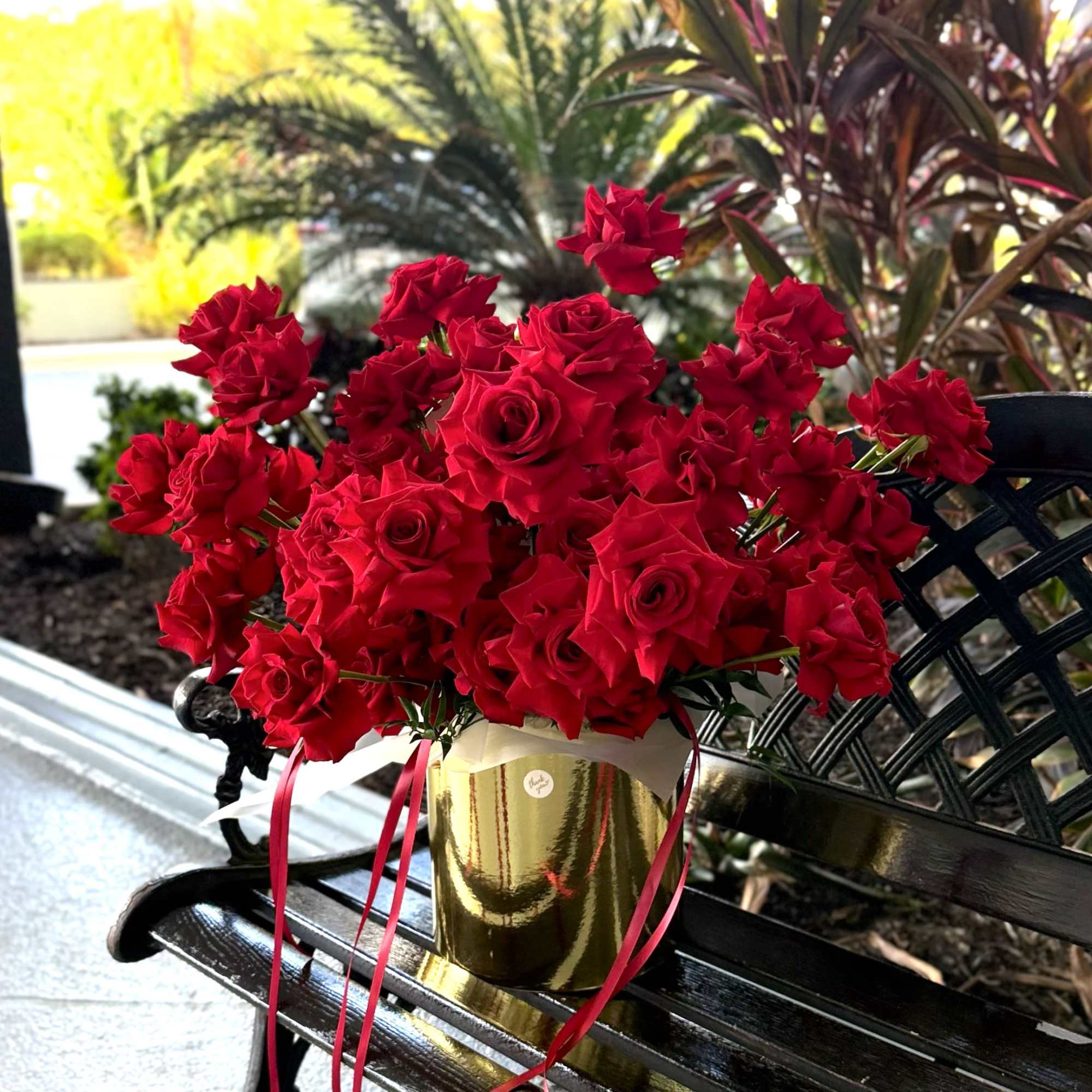 Velvet-red roses packed into a reflective gold cylindrical box create an immediate