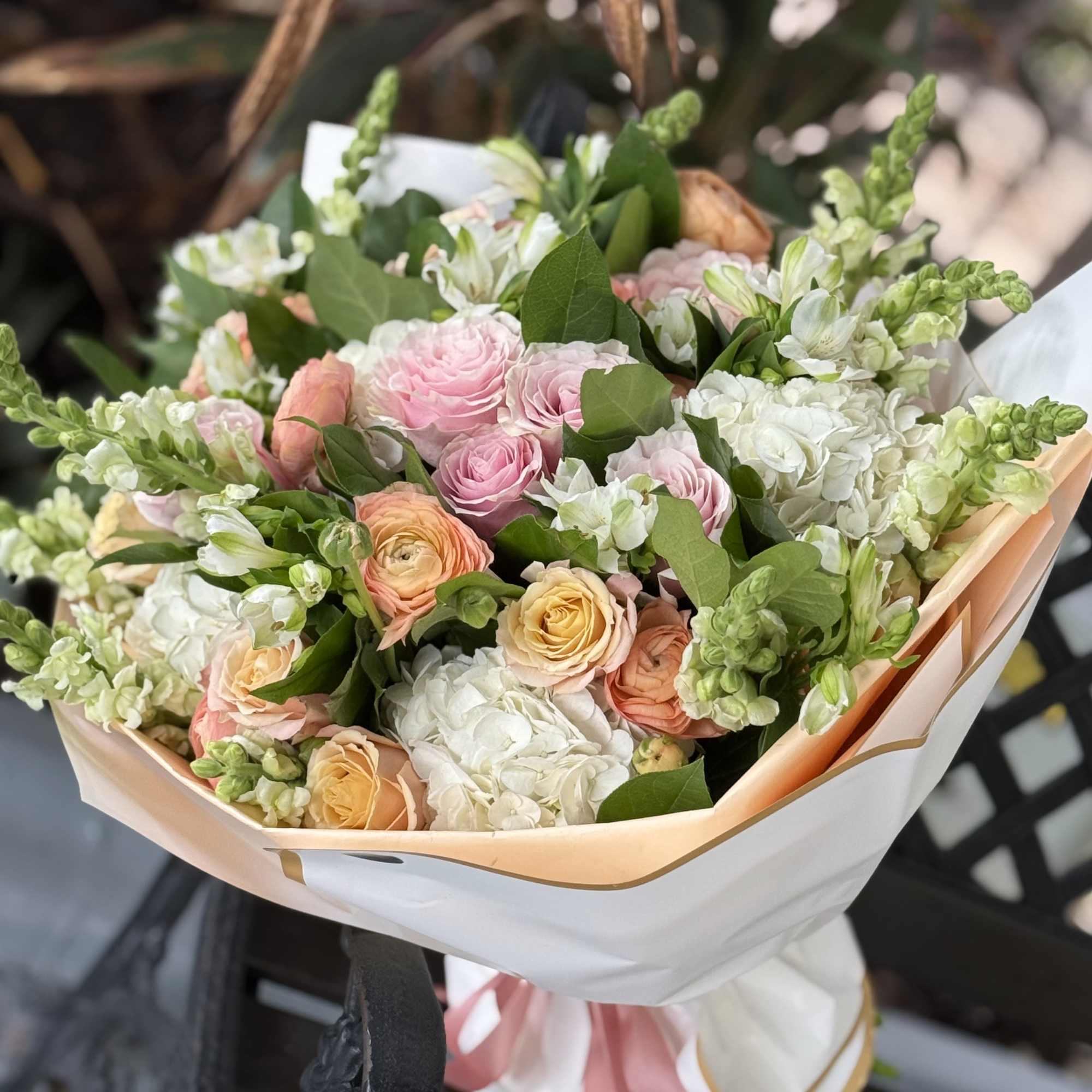 A lush hand-tied bouquet in a soft pastel palette of pink, peach