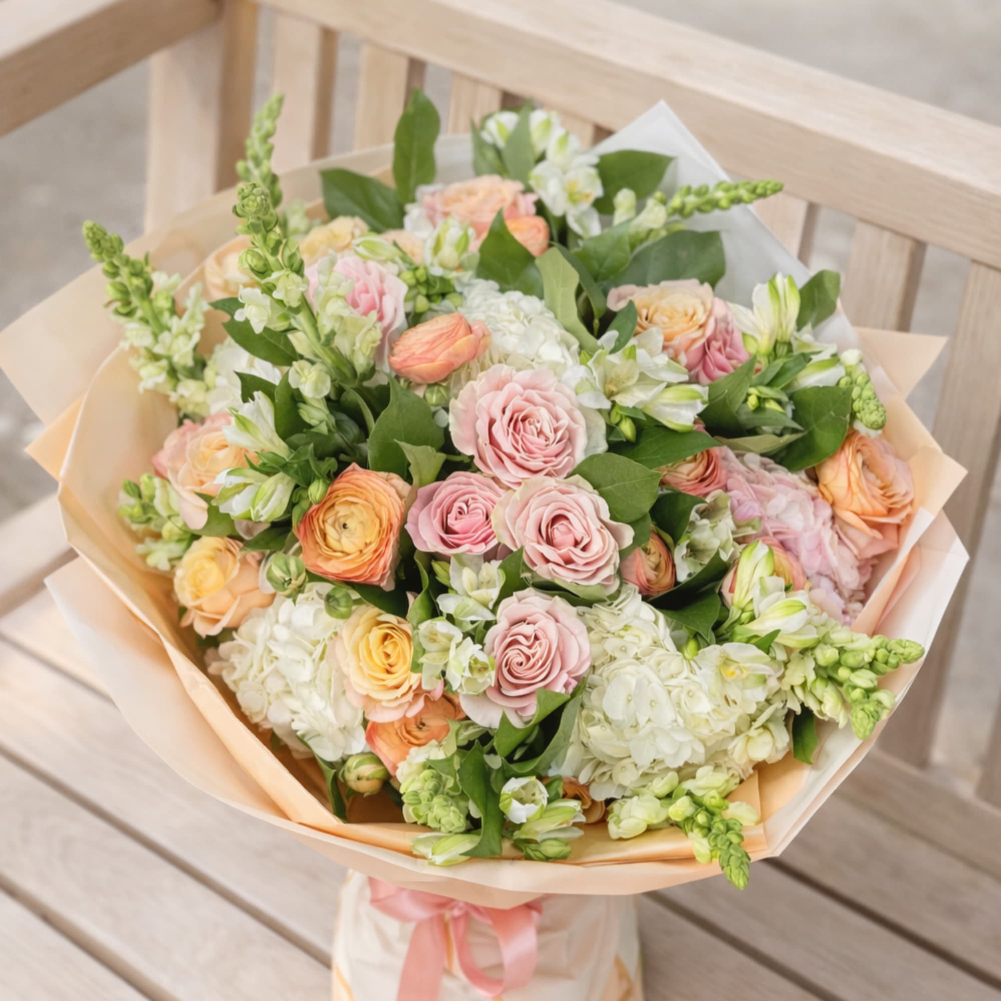 A lush hand-tied bouquet in a soft pastel palette of pink, peach