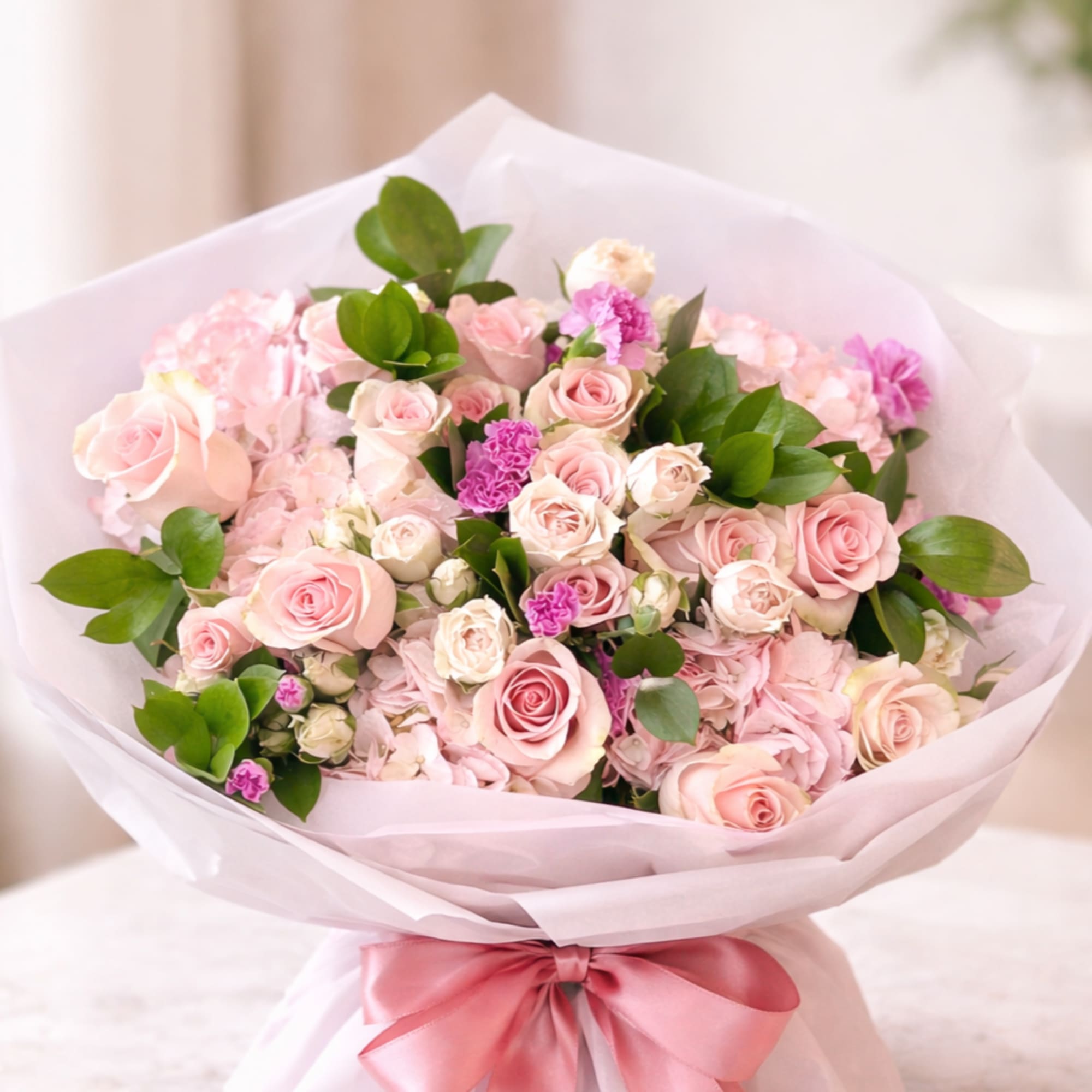 A lush, rounded hand-tied bouquet in soft shades of blush pink, cream