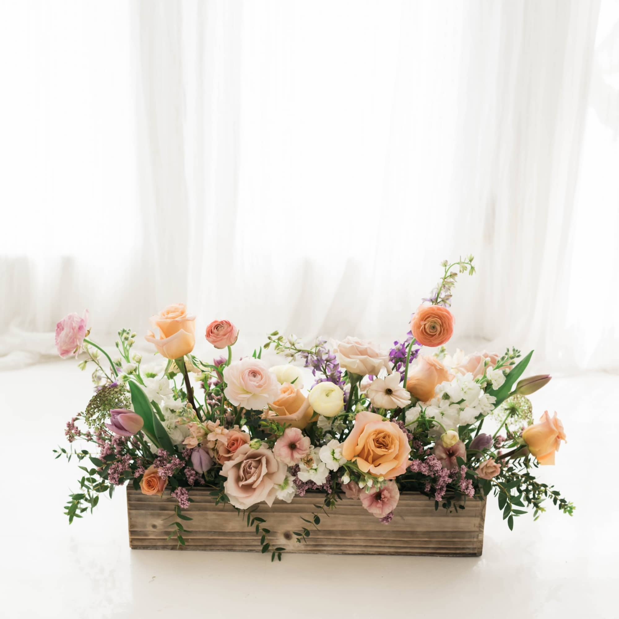 Low floral arrangement in a wooden box with peach, pink, and white blooms