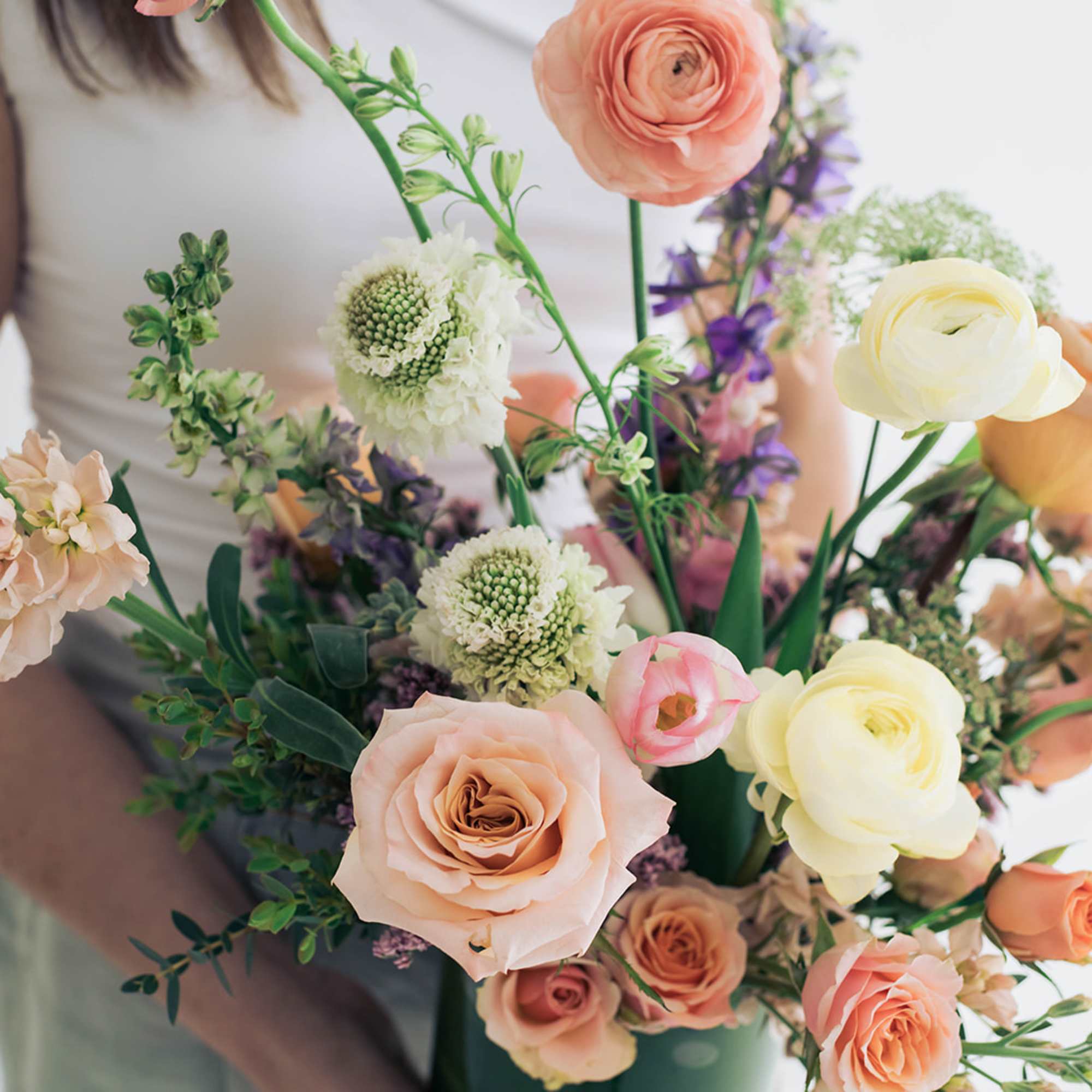 Handheld bouquet of peach, cream, and purple flowers