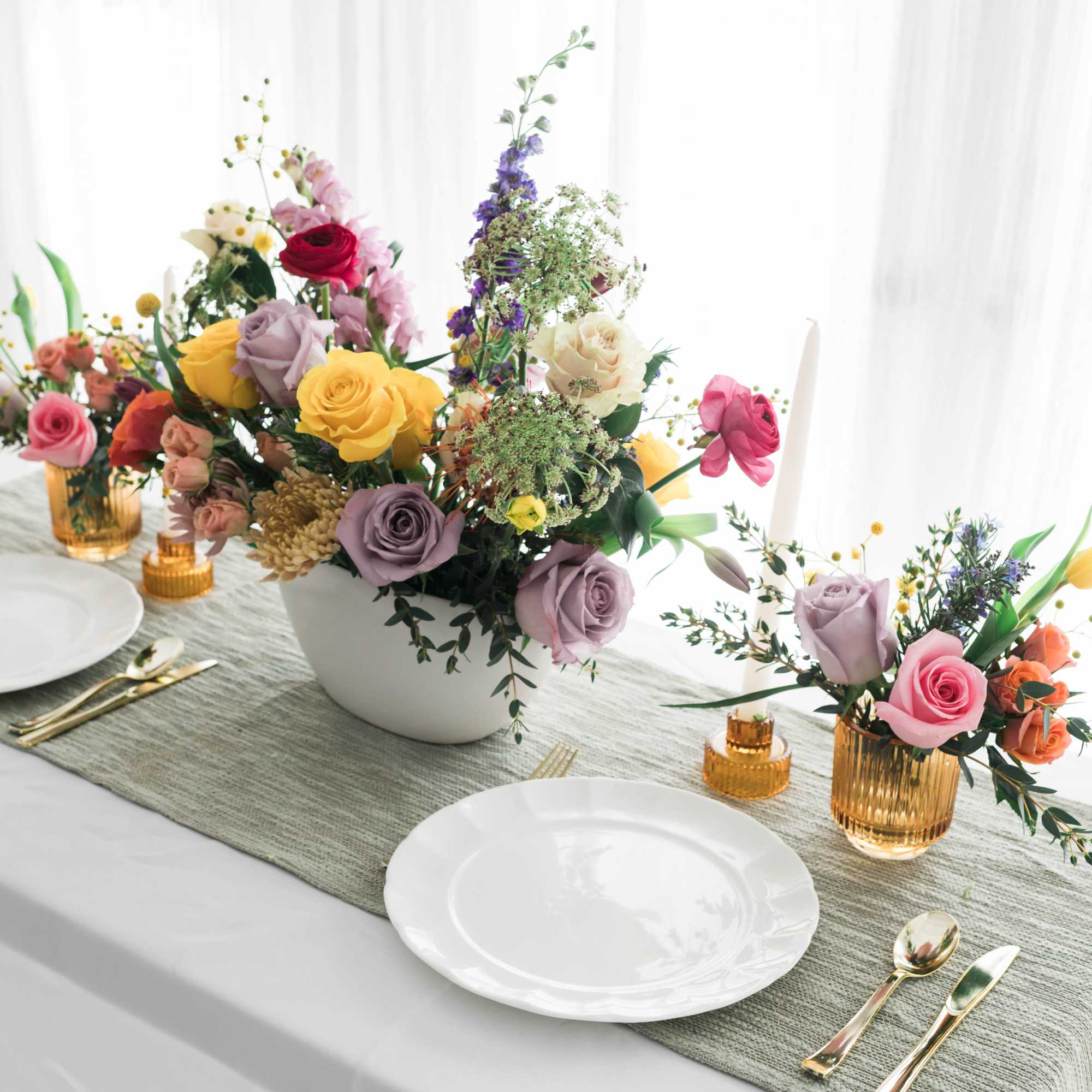 Floral table centerpiece with roses in a white bowl and small amber vases