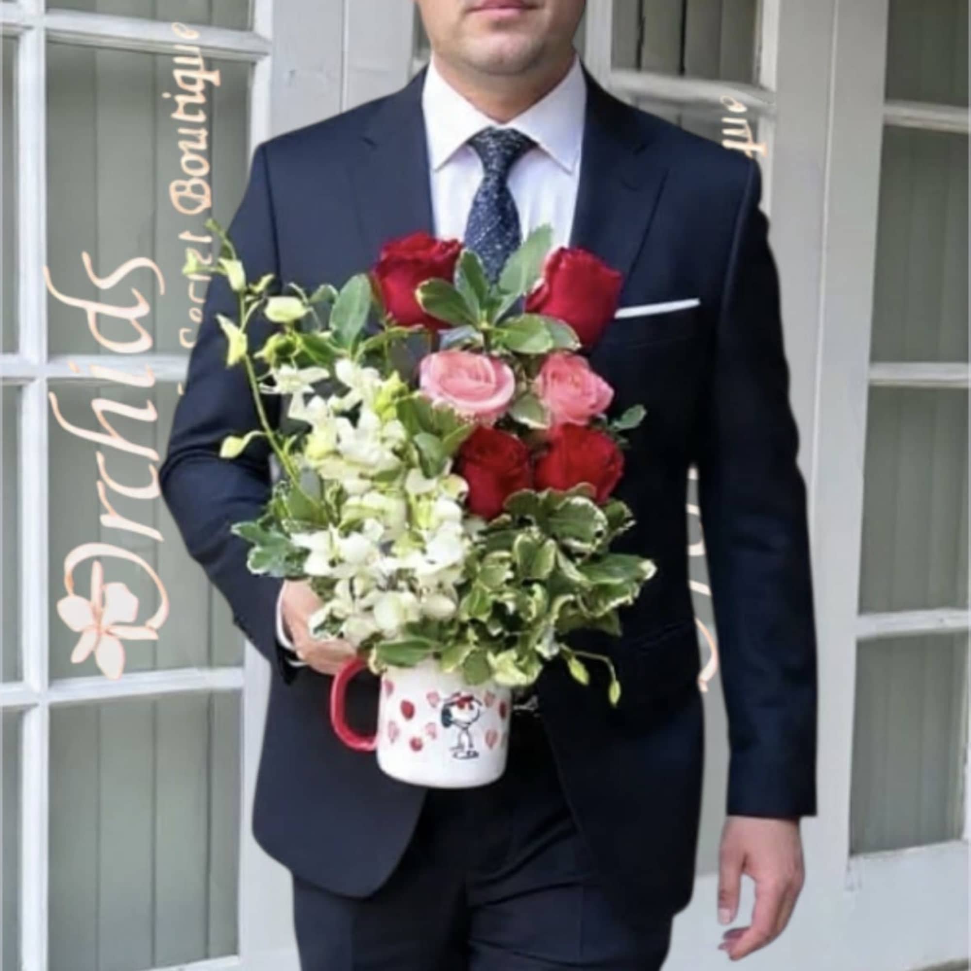 Man in a suit holding a mug arrangement of red and pink roses