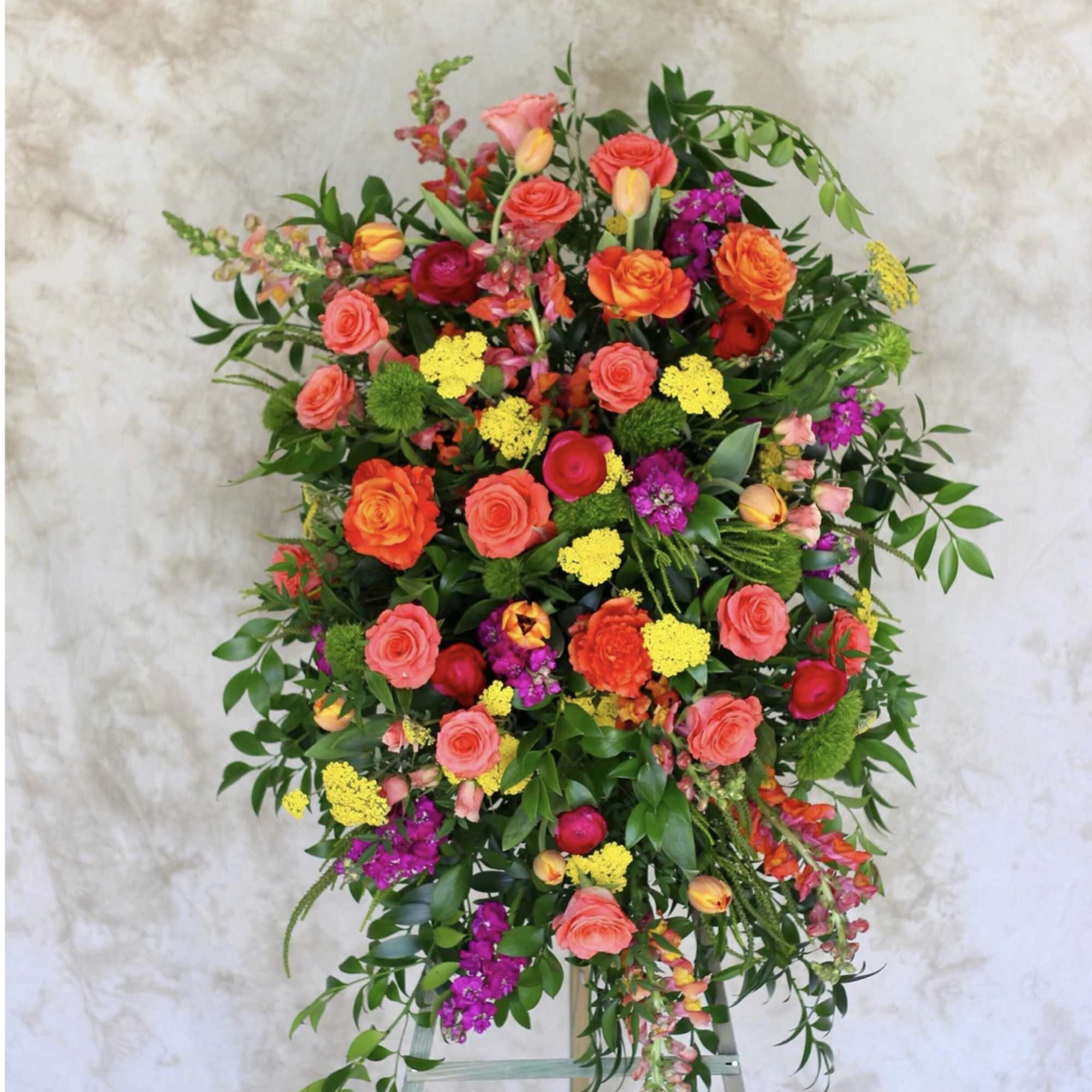 Bright standing spray of orange roses, yellow blooms, and pink and purple flowers on an easel