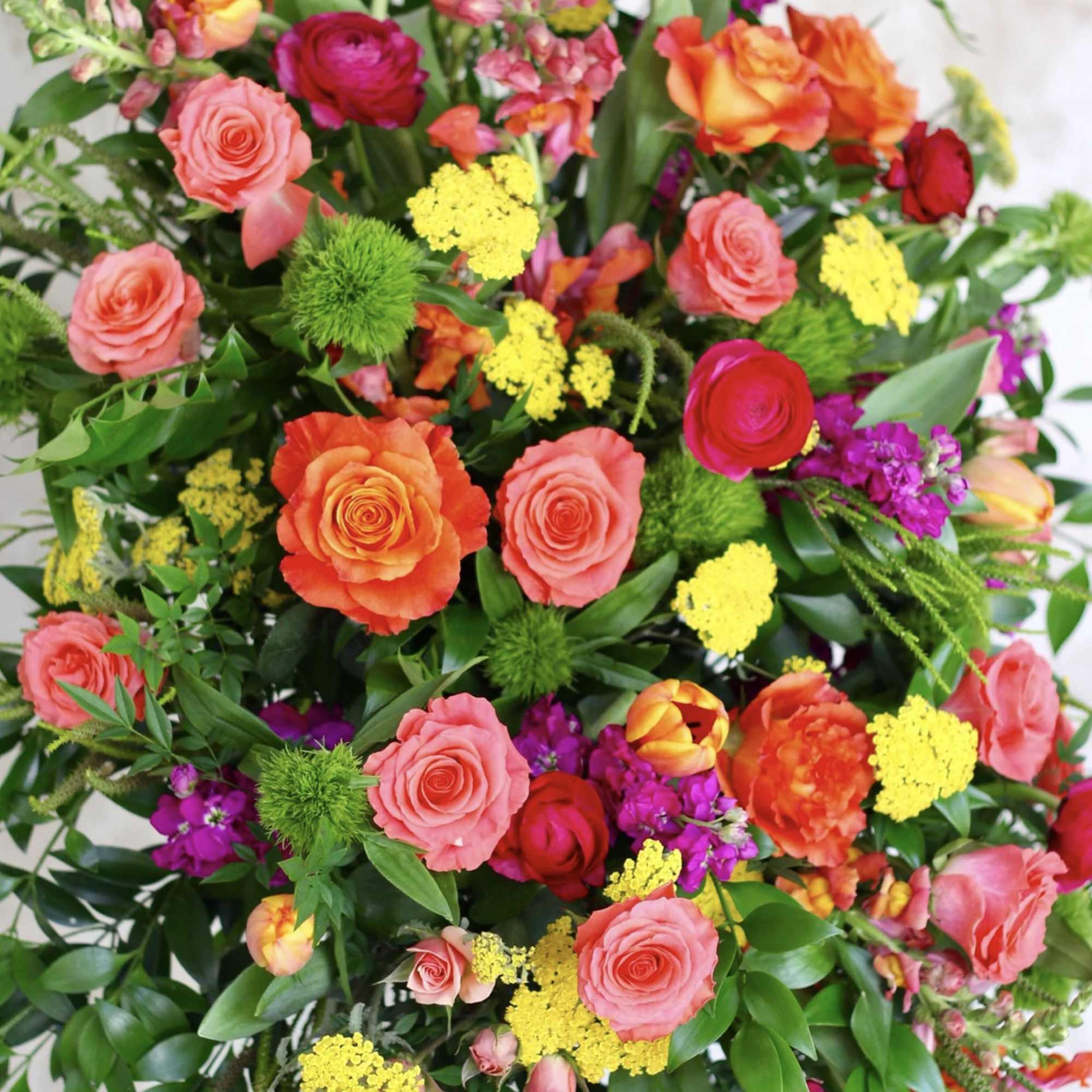 Tall, vibrant arrangement of orange and pink roses with yellow accents and mixed bright blooms