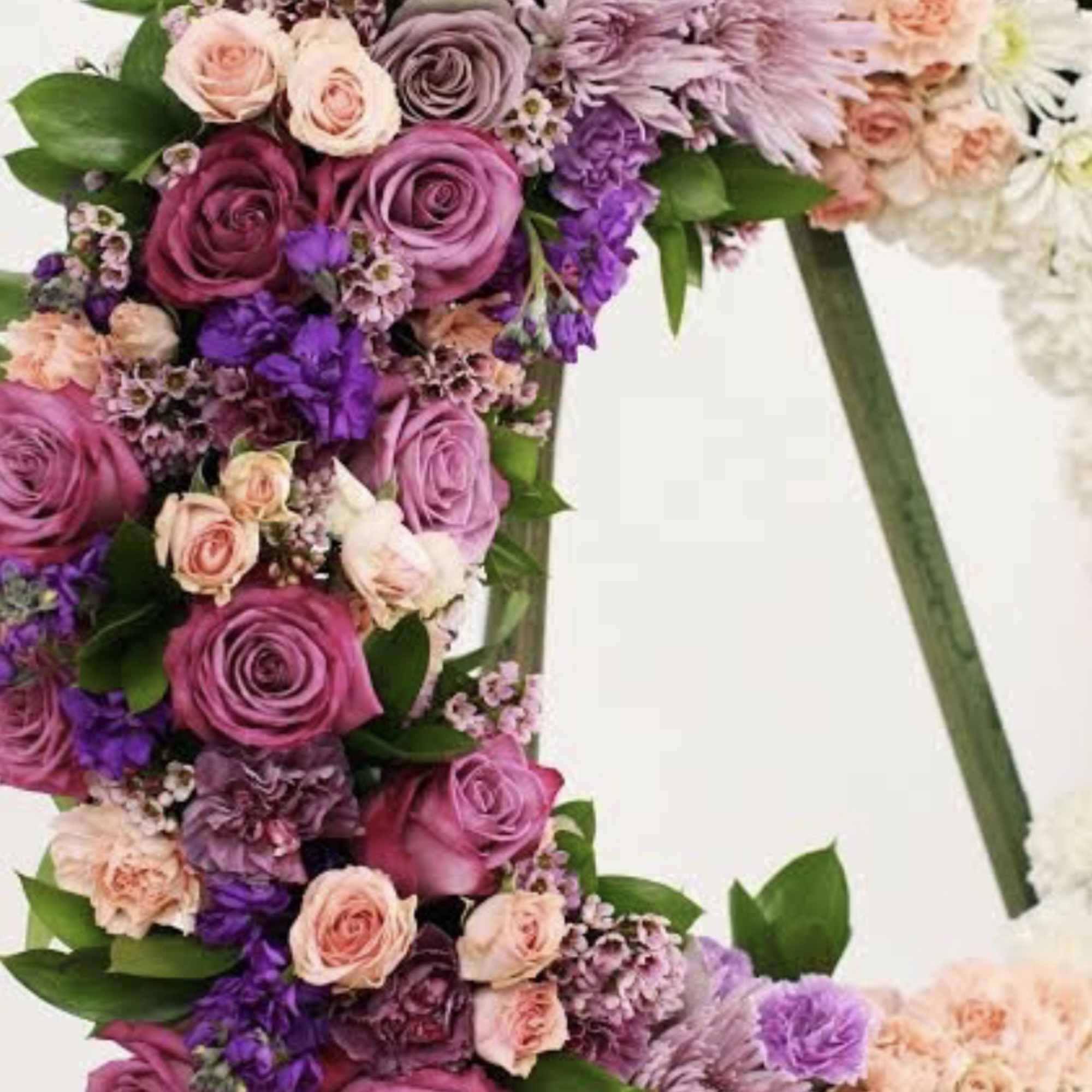 Standing wreath of pink and purple roses, carnations, and mums on an easel.