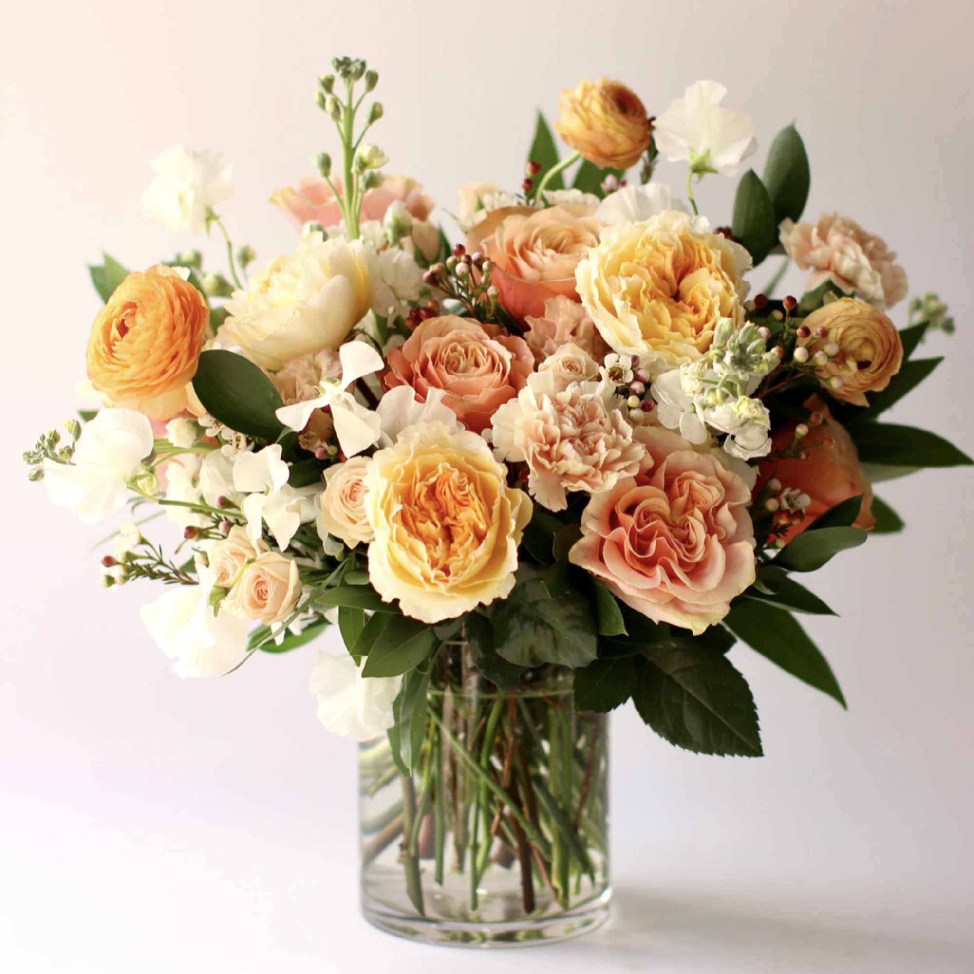 Peach and yellow rose arrangement with white accents in a clear glass vase.