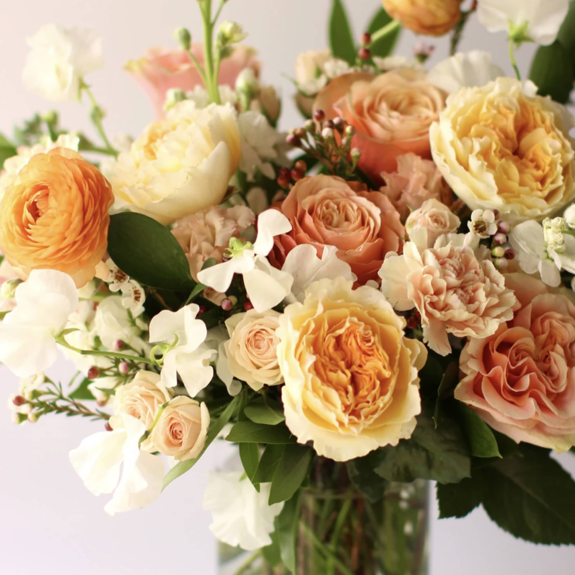 Peach and yellow rose and ranunculus arrangement in a clear glass vase
