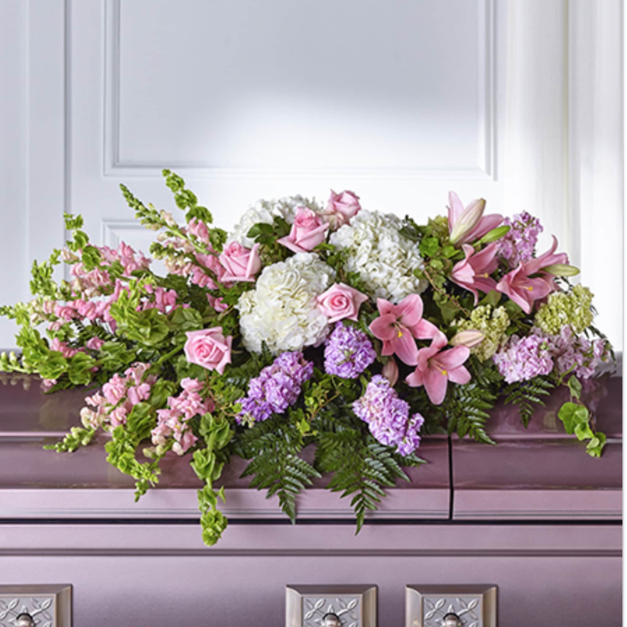 Pastel pink and white casket spray with roses, lilies, and hydrangeas on a lavender casket.