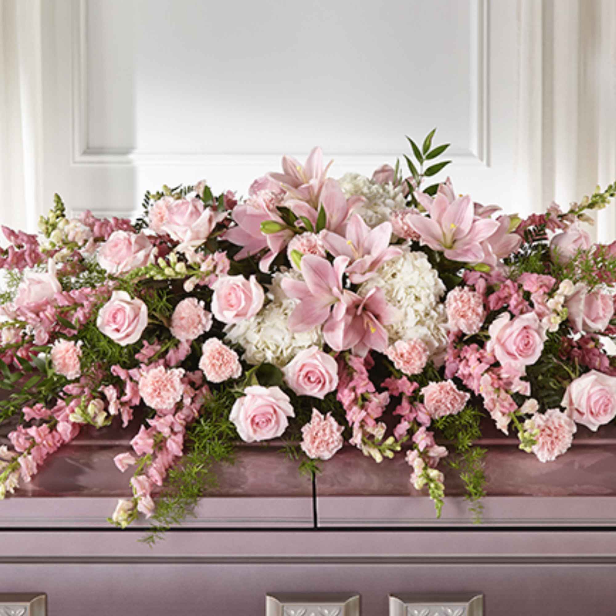 Pink lilies, roses, and carnations with white blooms arranged as a casket spray on a mauve casket