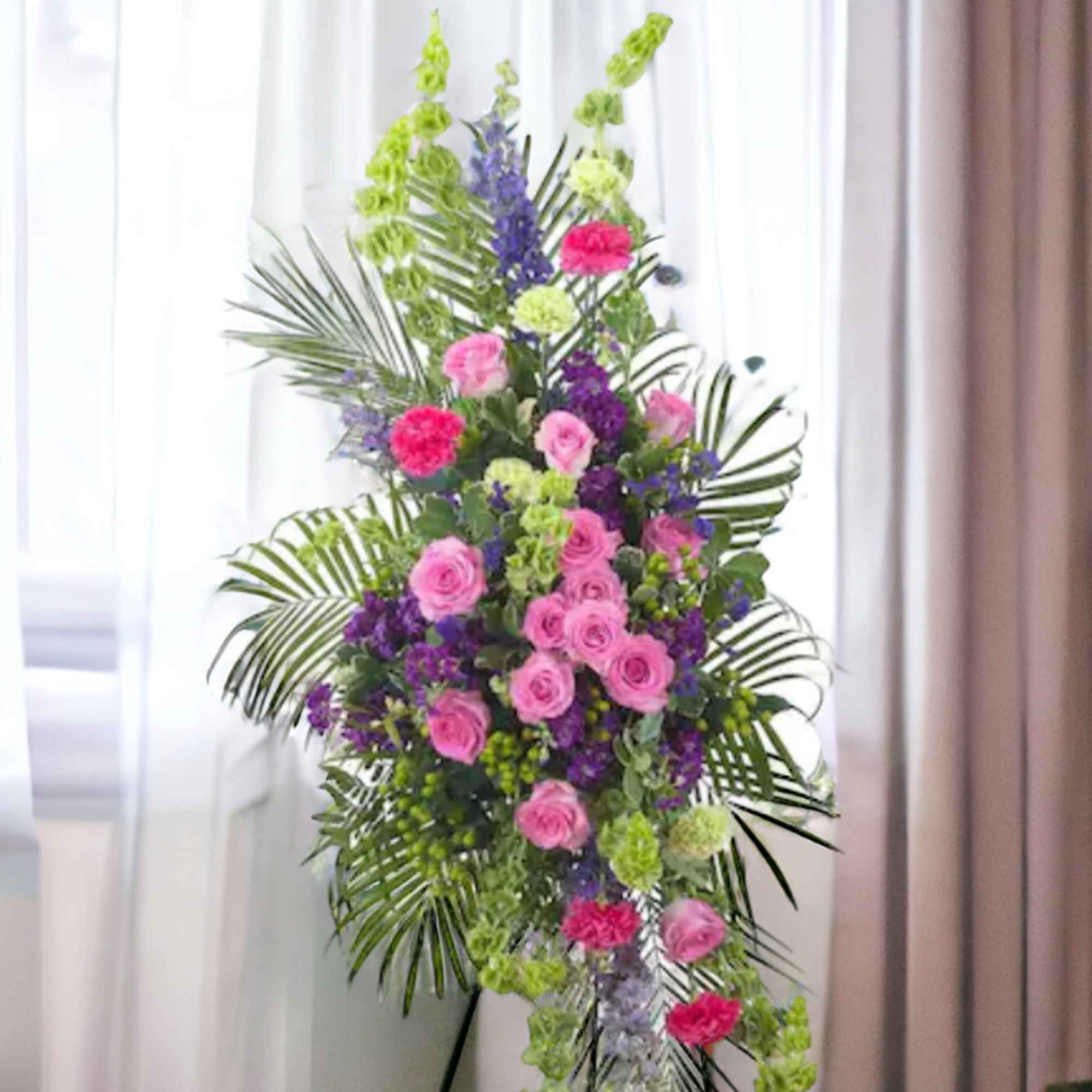 Tall standing spray with pink roses, purple flowers, and green accents on an easel.