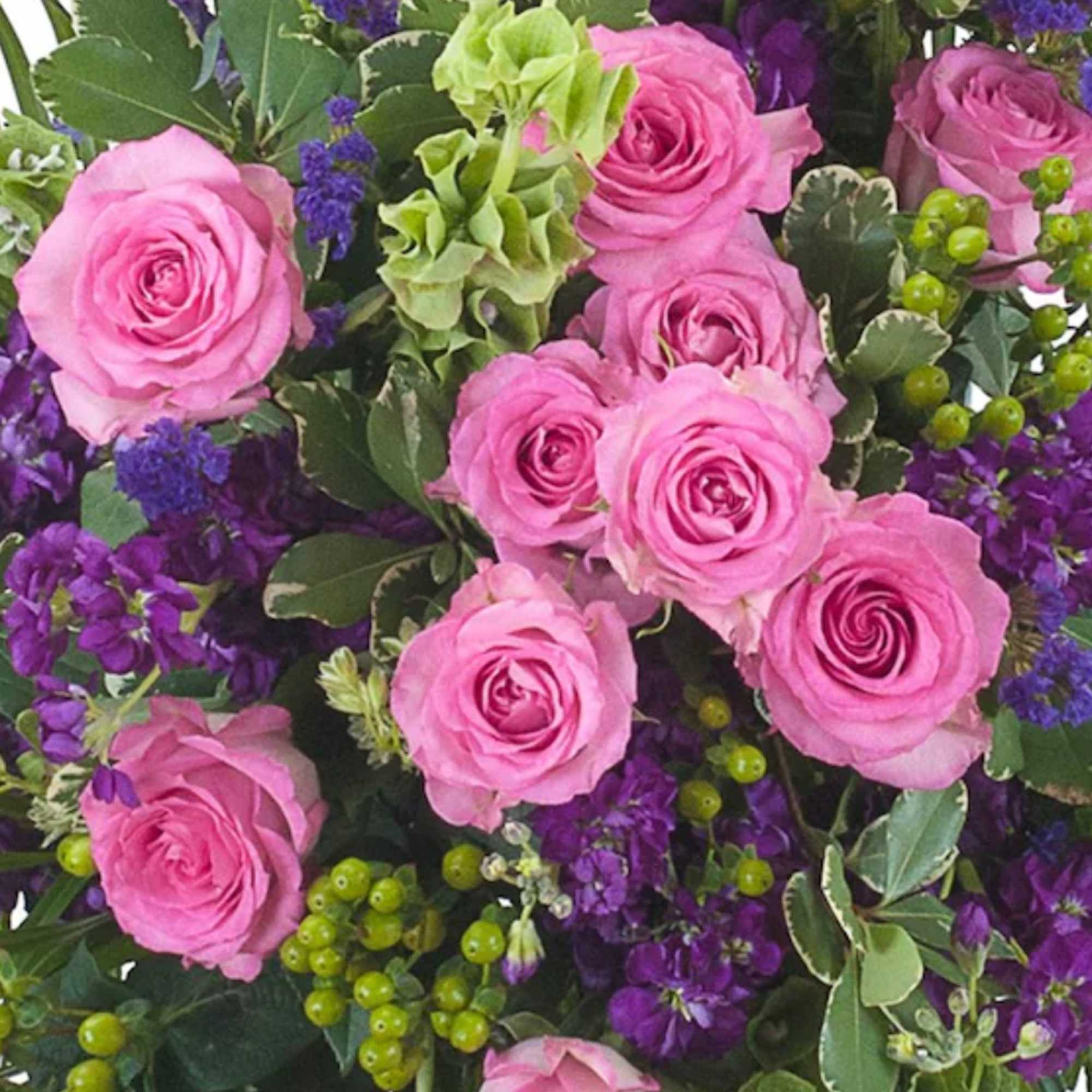 Close-up of pink roses with purple flowers and green berries in a dense floral arrangement
