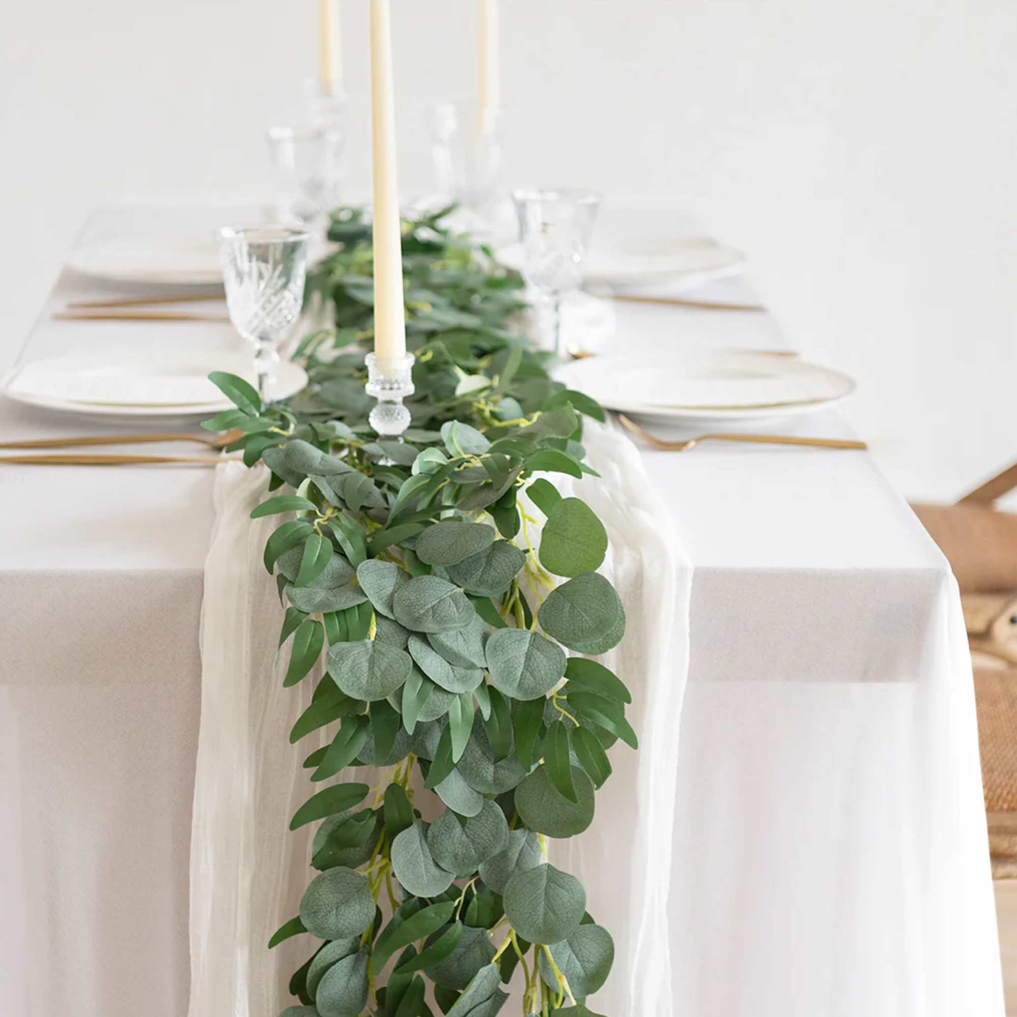 White table with a long eucalyptus greenery garland and tall ivory taper candles.