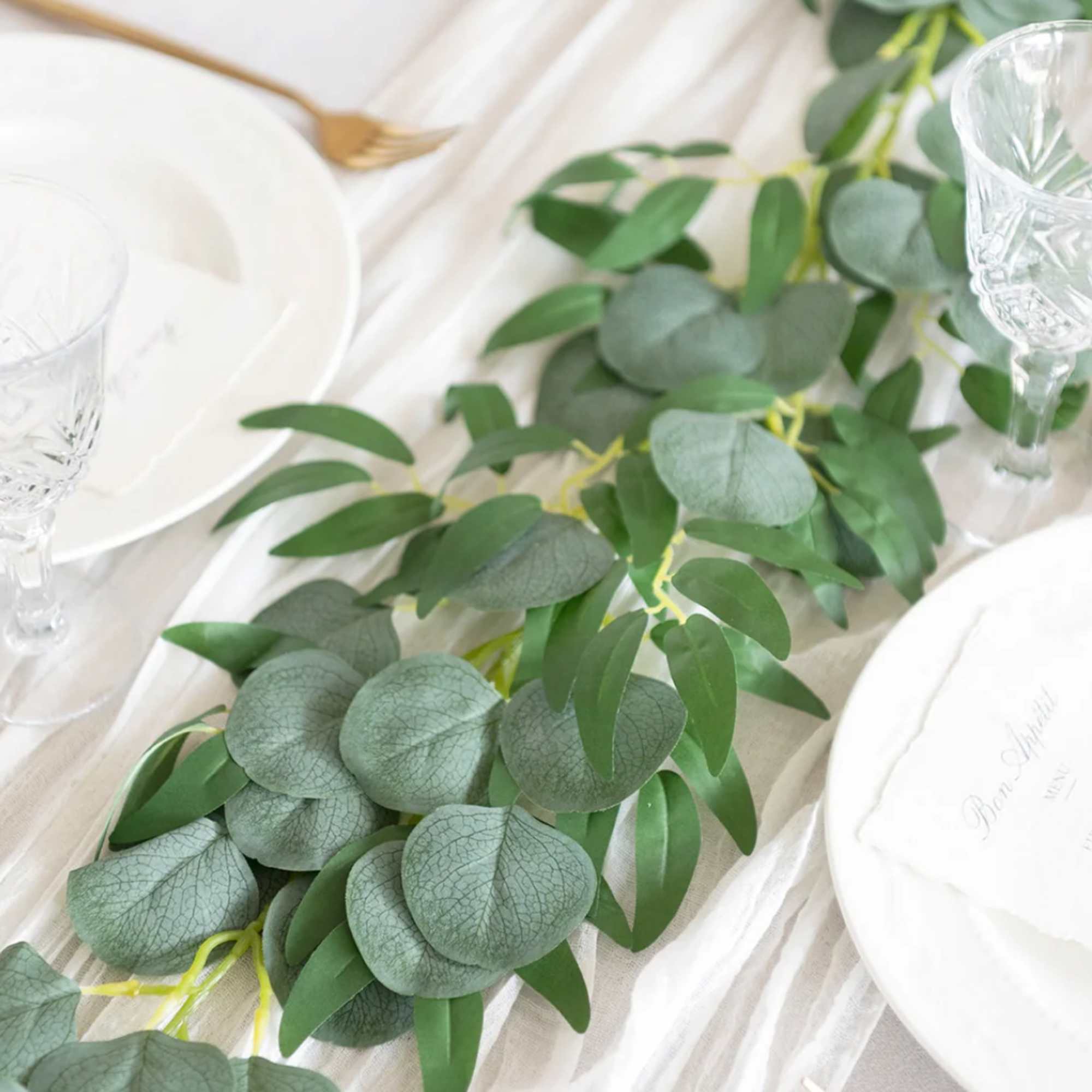 Green leafy garland running down a white table set with plates and crystal glasses