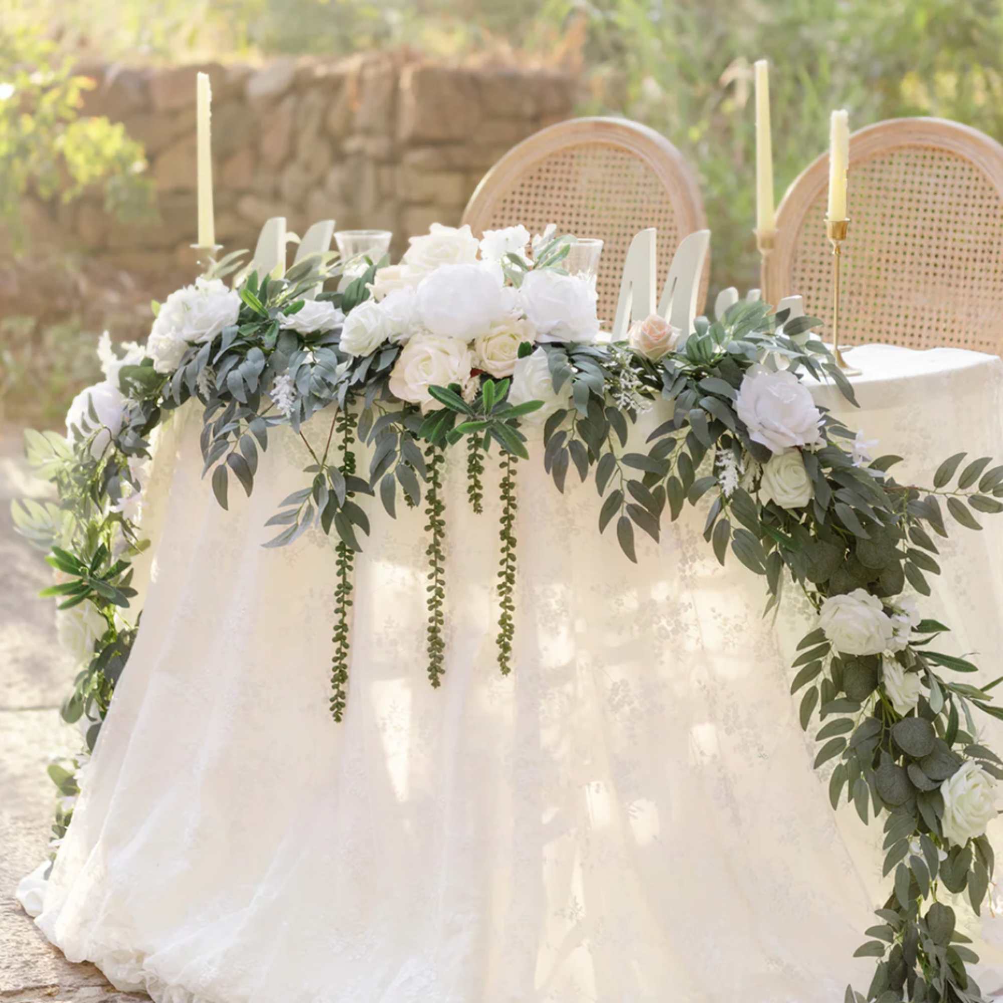 White floral garland with lush foliage draped across a sweetheart table with candles.