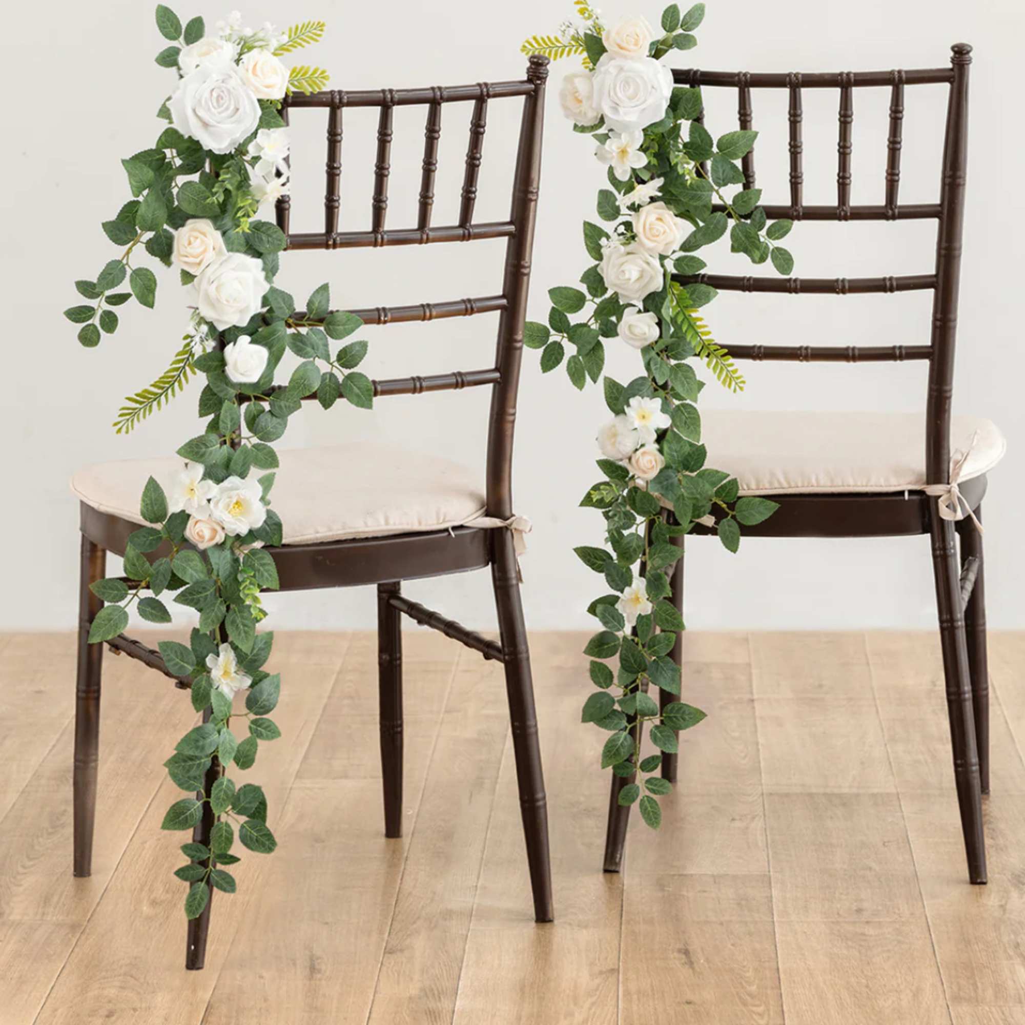 Pair of dark chairs decorated with cascading white and cream rose garlands with lush green foliage