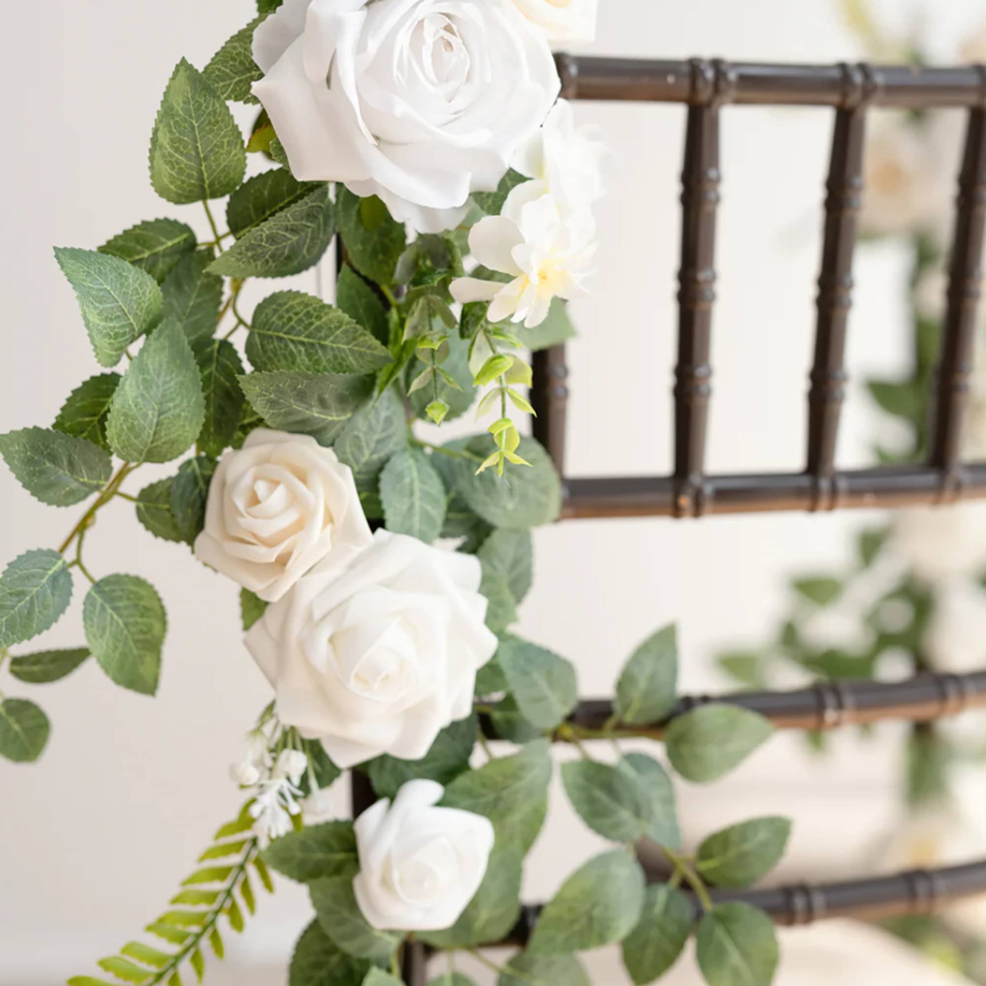 Silk white rose garland with greenery draped over a dark wooden chair back