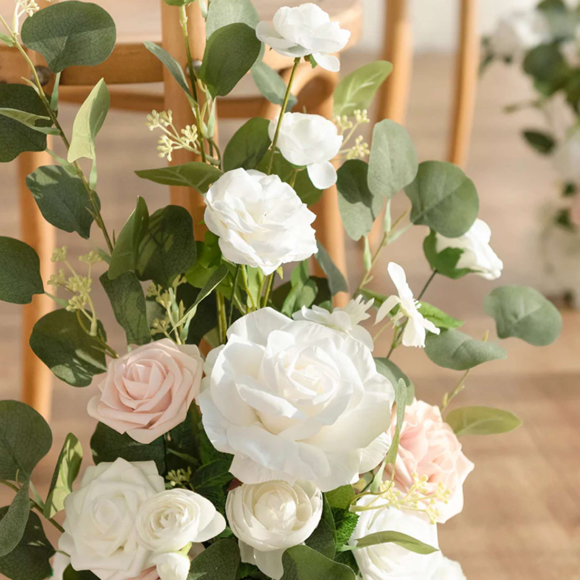 Floor arrangement of white and blush roses with abundant greenery beside wooden chairs