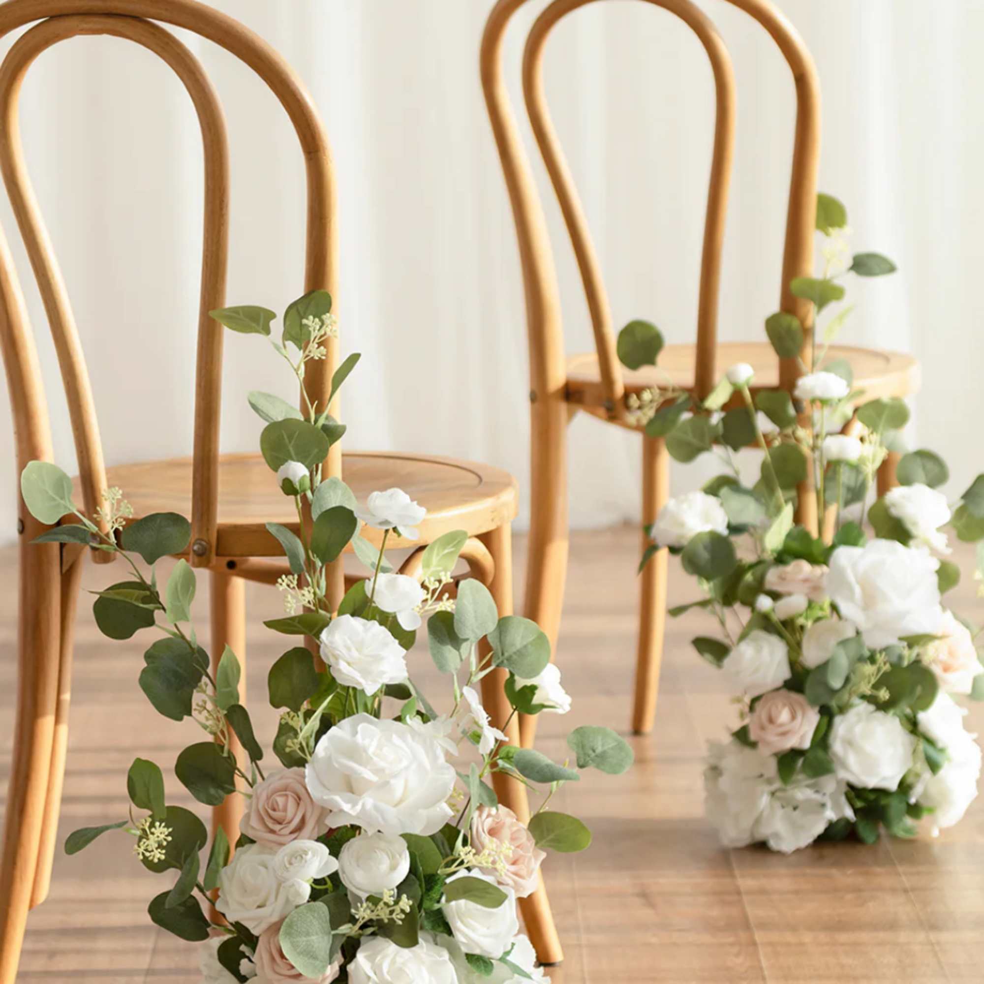 White and blush rose aisle arrangements with greenery beside wooden chairs