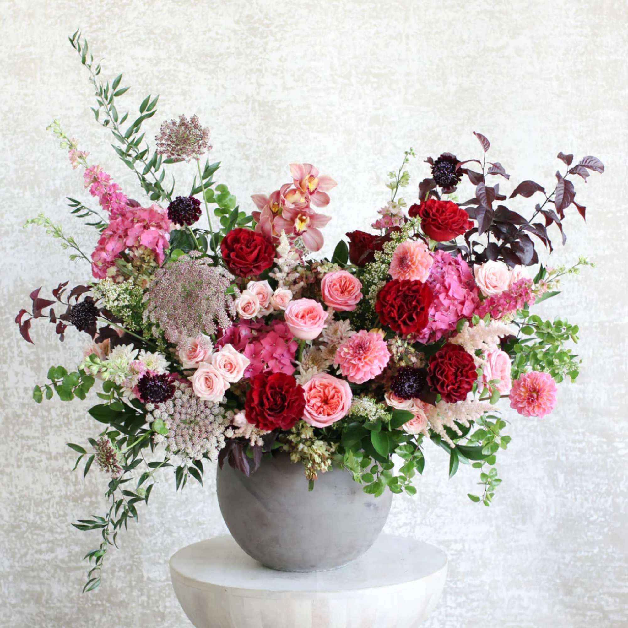 Large pink and red flower arrangement with roses and hydrangeas in a round gray vase
