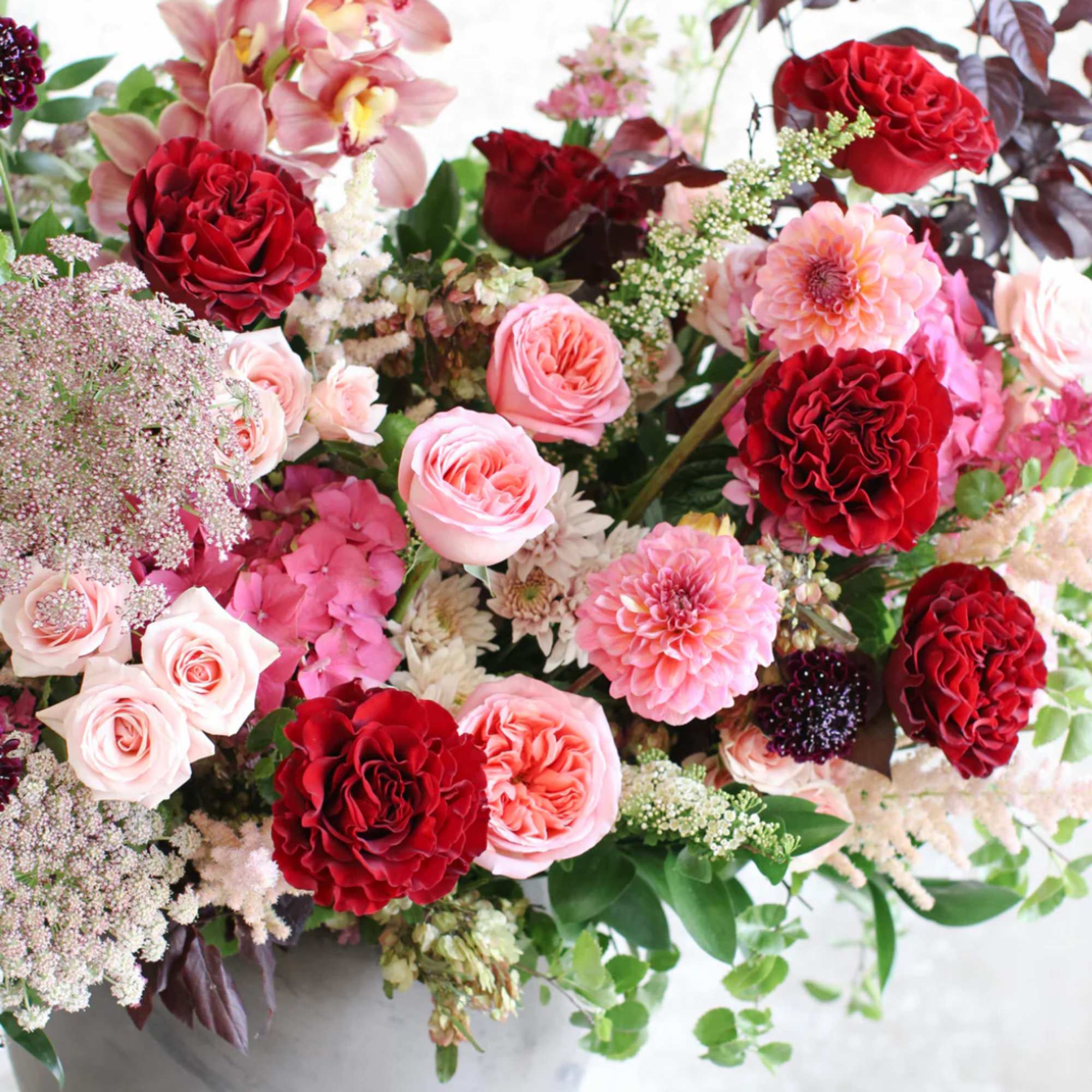 Lush arrangement of red and pink roses, dahlias, orchids and mixed blooms in a gray round vase